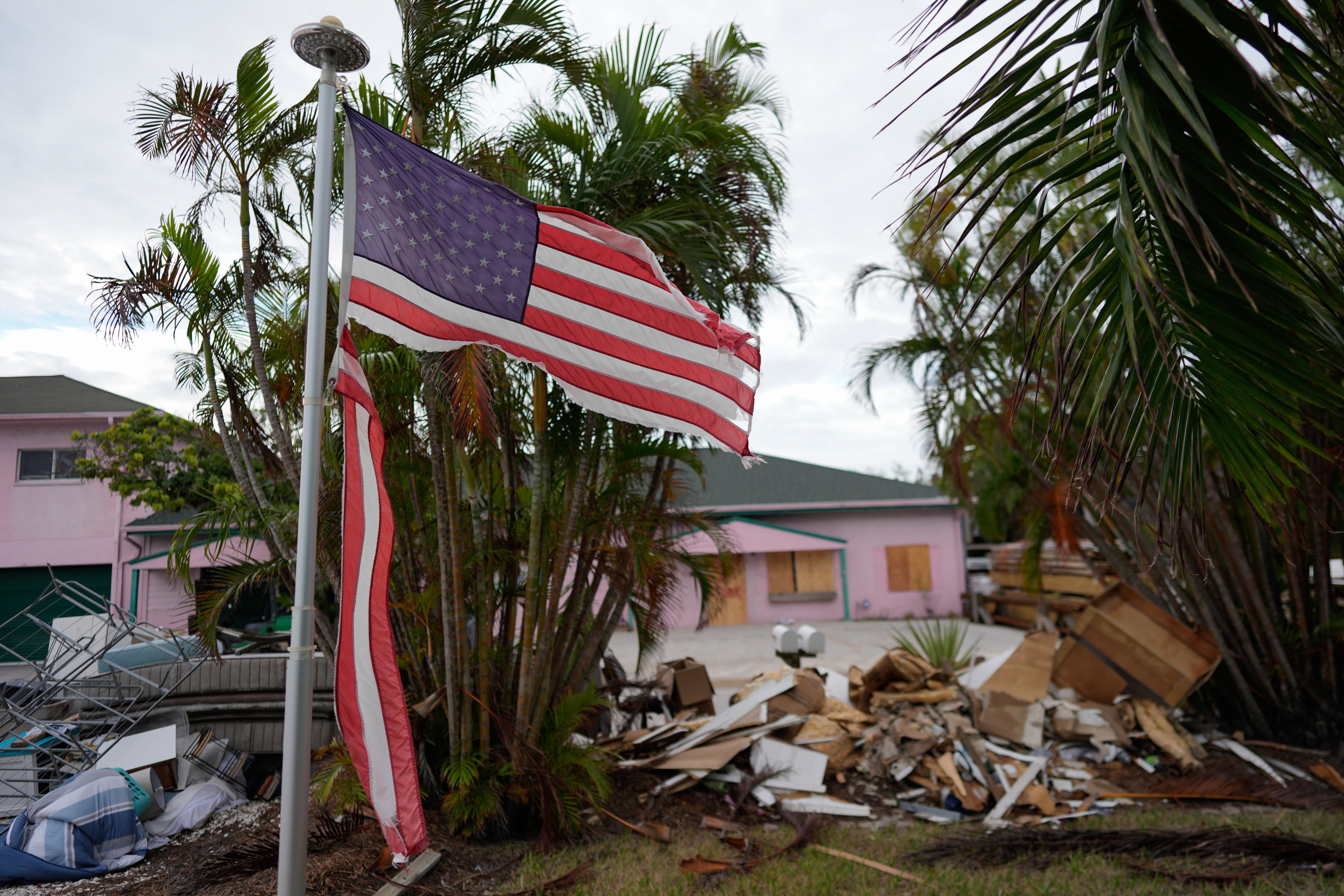 A tattered American flag flaps outside a home as furniture and household items damaged by Hurricane Helene flooding sit piled along the street awaiting pickup, ahead of the arrival of Hurricane Milton, in Holmes Beach on Anna Maria Island, Florida, in early October