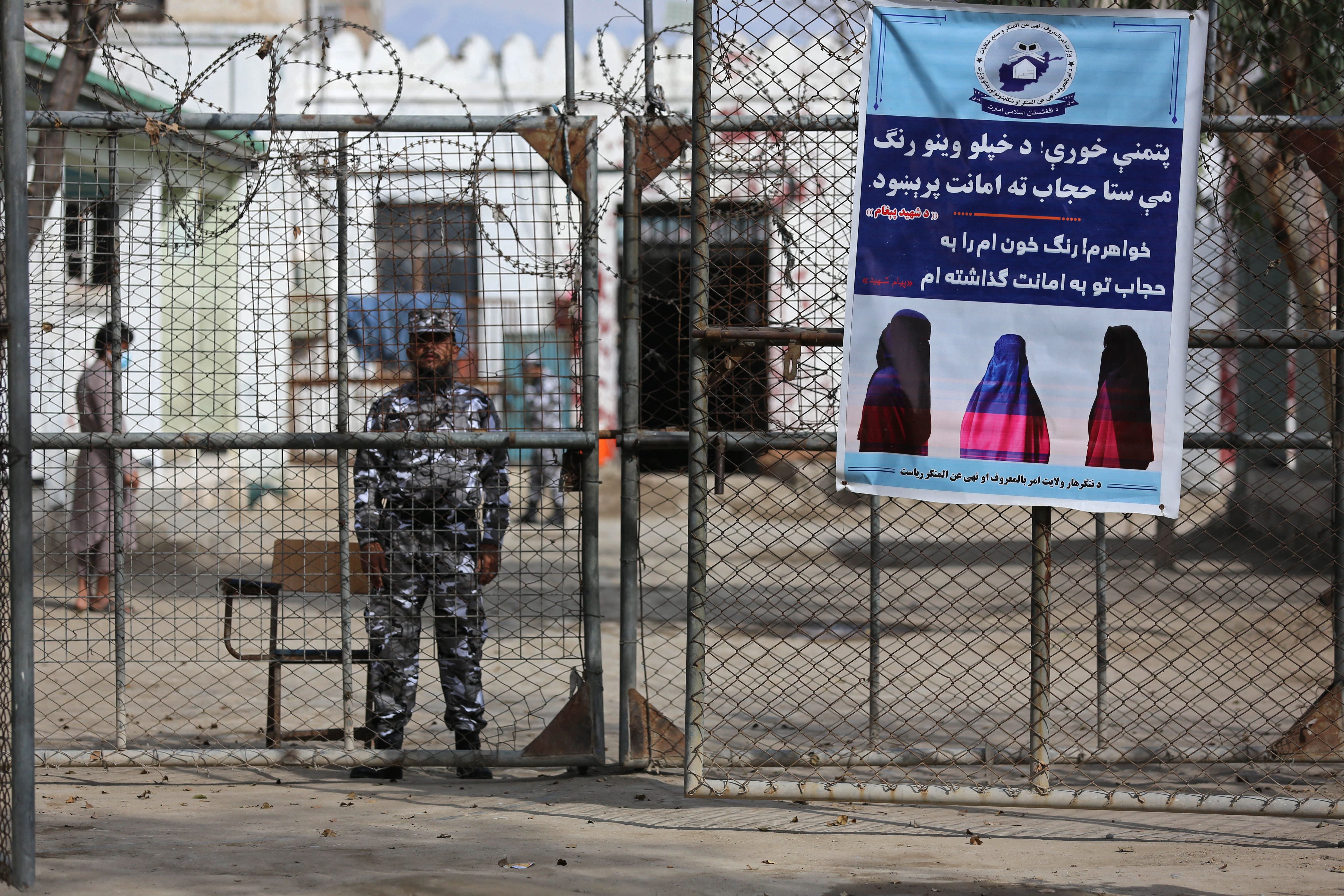 A Taliban guard at a prison in Jalalabad stands next to a poster ordering women to cover themselves with a hijab