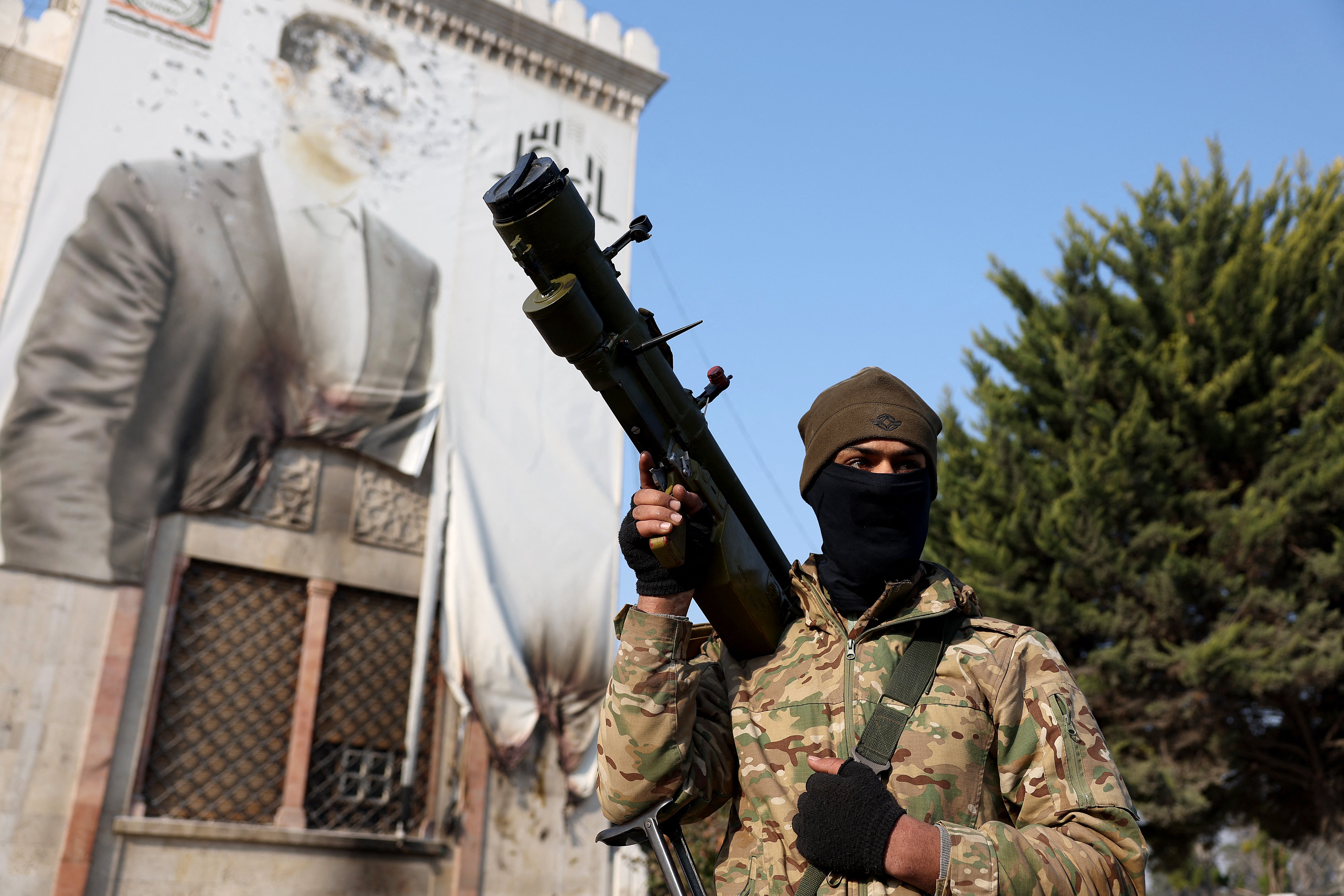 An anti-government fighter holds a weapon as he keeps position near a defaced portrait of Assad, in the city of Hama