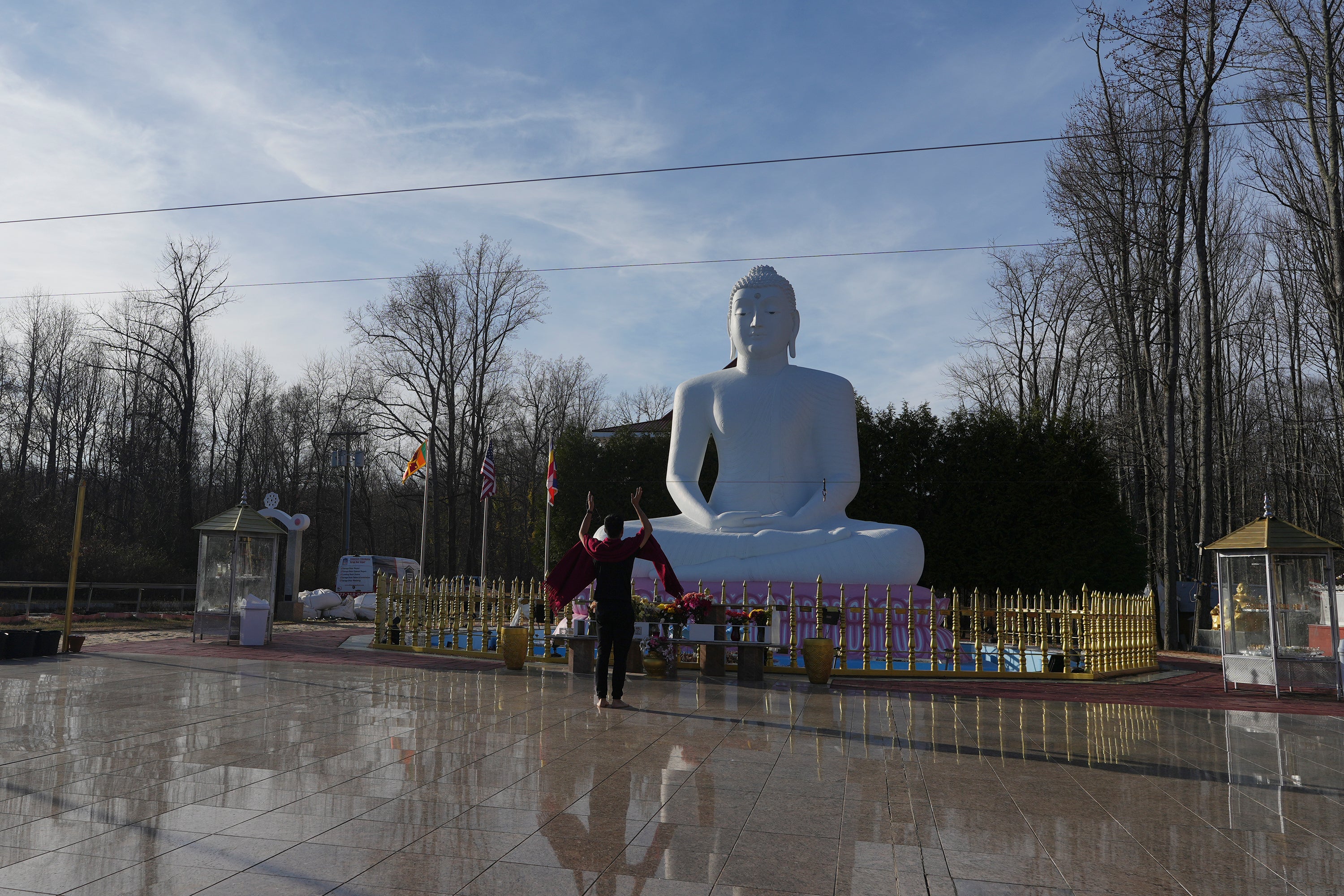 Daniel Choi lifts his arms during his chanting and meditation practice in front of a statue of the Buddha