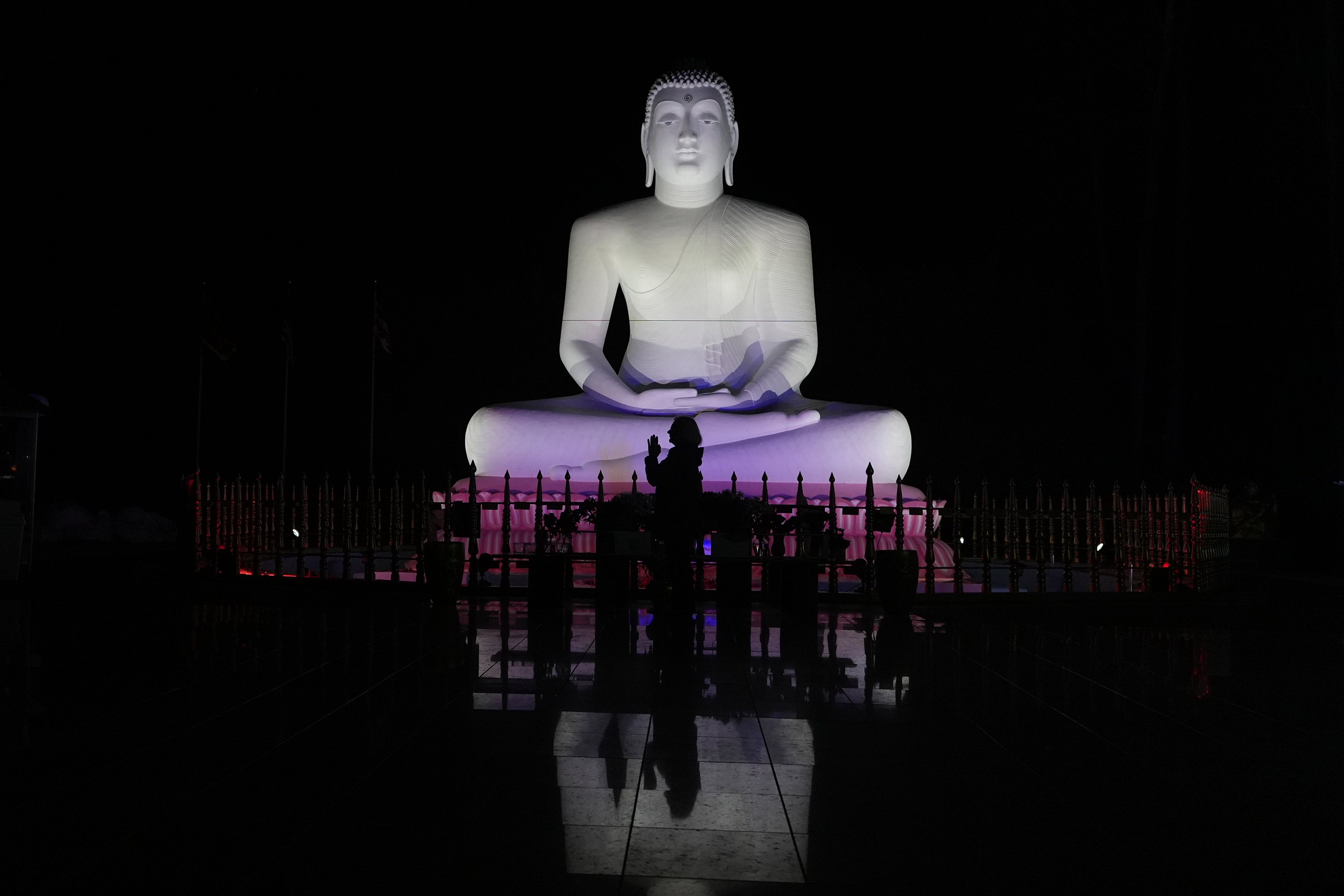 Carol Kruhen lifts up her pressed palms next to a statue of the Buddha