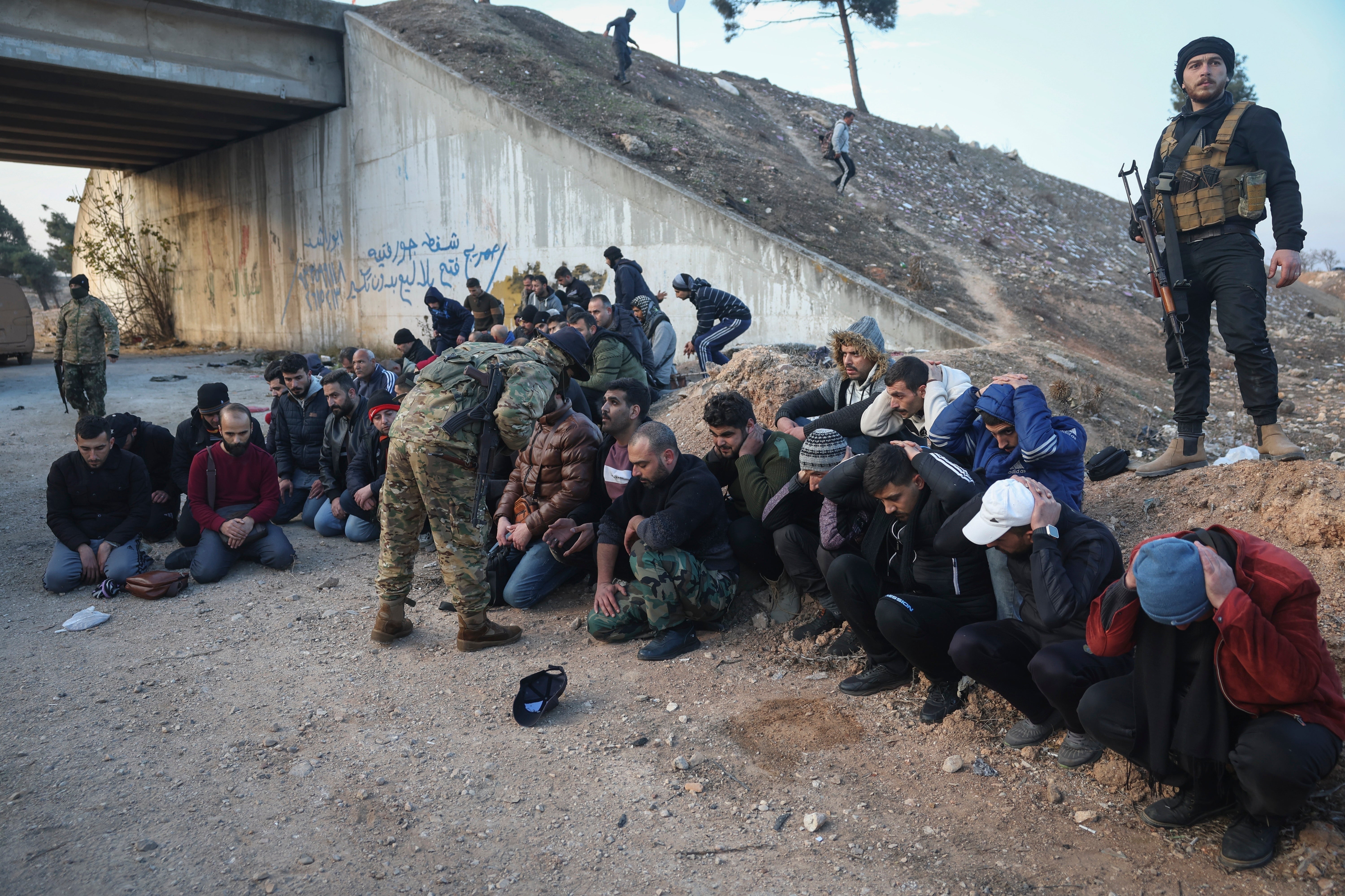 Government soldiers and allies sit on the ground as they are taken into custody by rebels on the road between Homs and Damascus