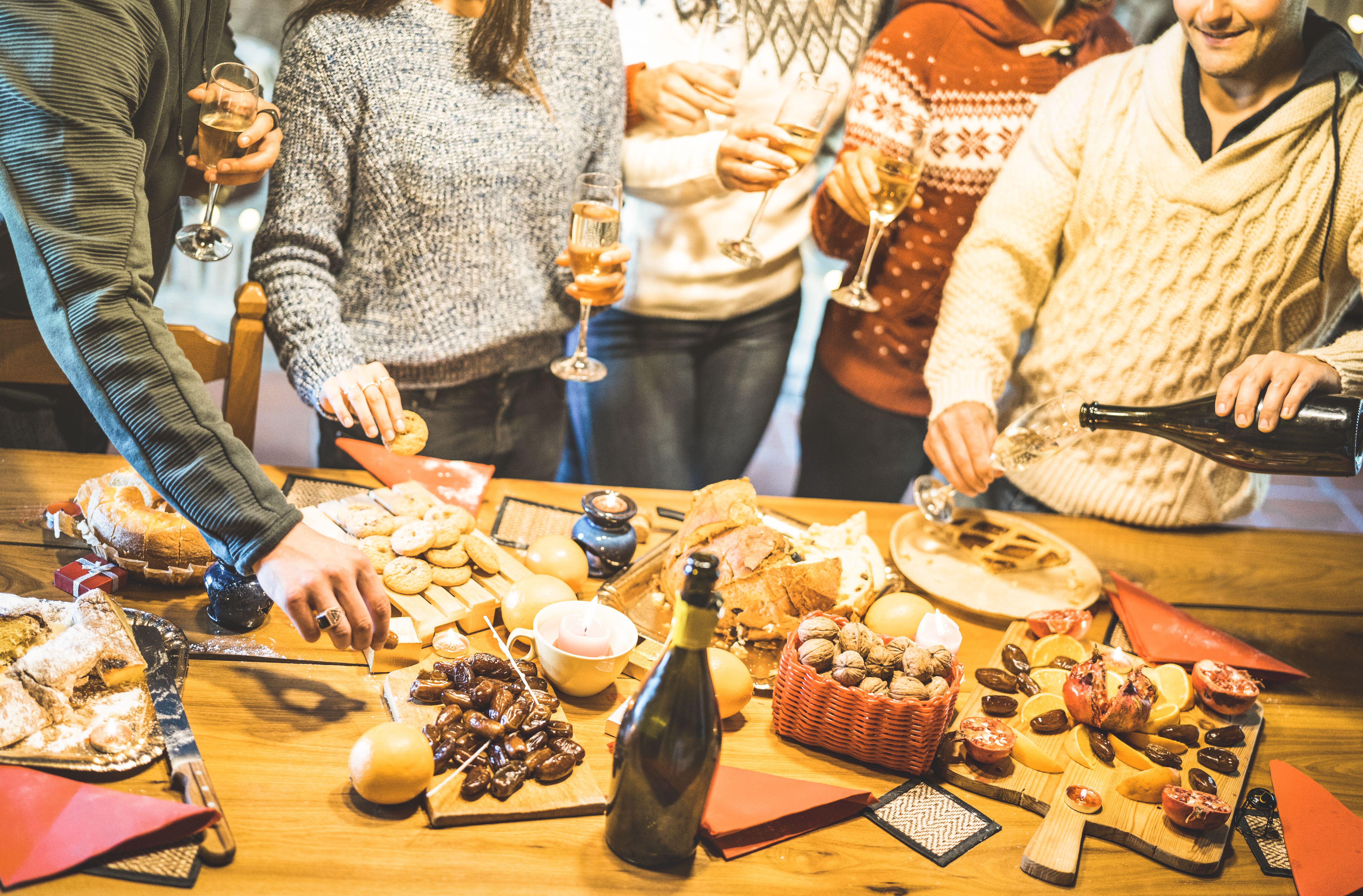 Side view of friends group tasting christmas sweets food and having fun at home drinking champagne sparkling wine – Winter holidays concept