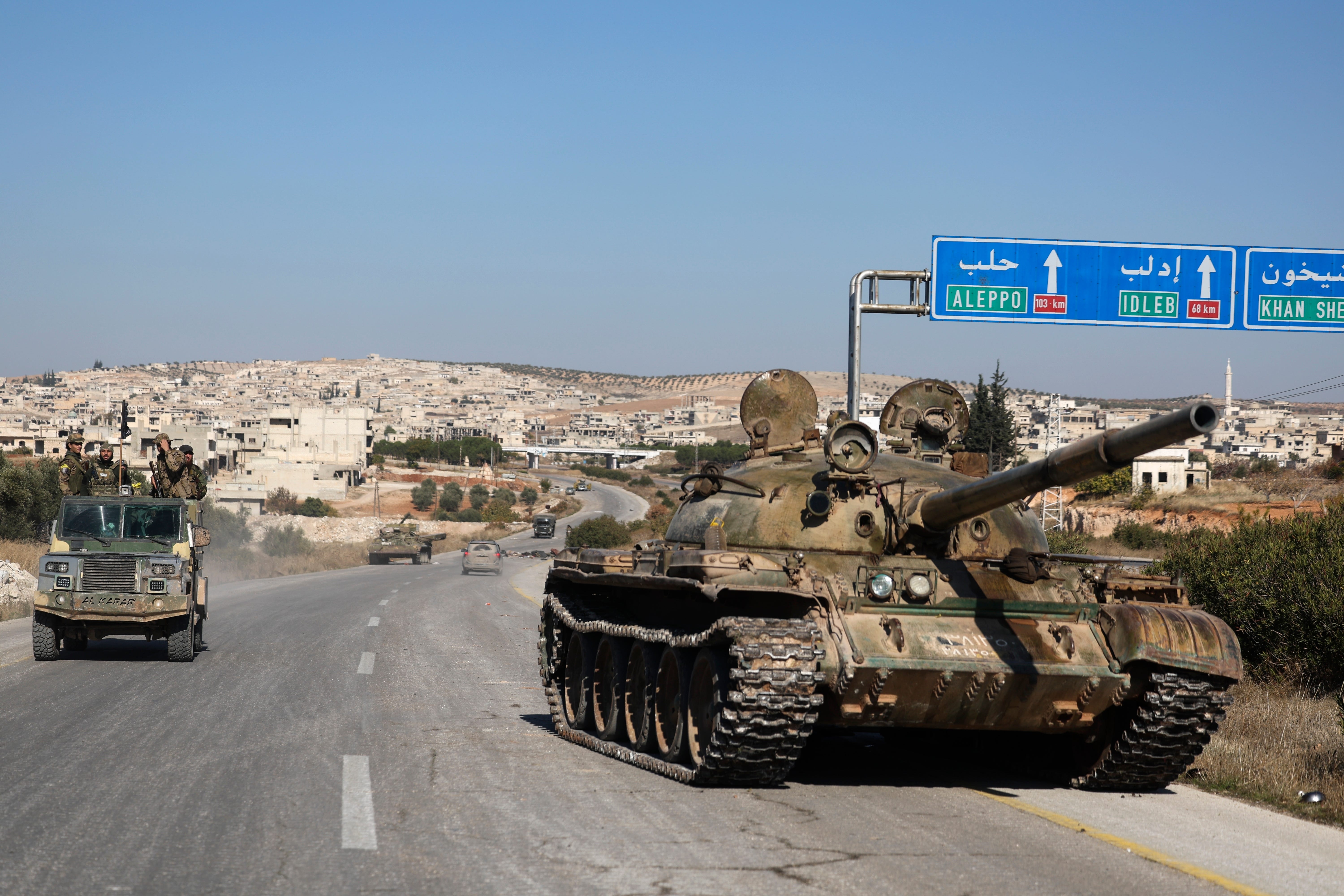 Syrian opposition fighters drive by an abandoned Syrian army armoured vehicle (Ghaith Alsayed/AP)