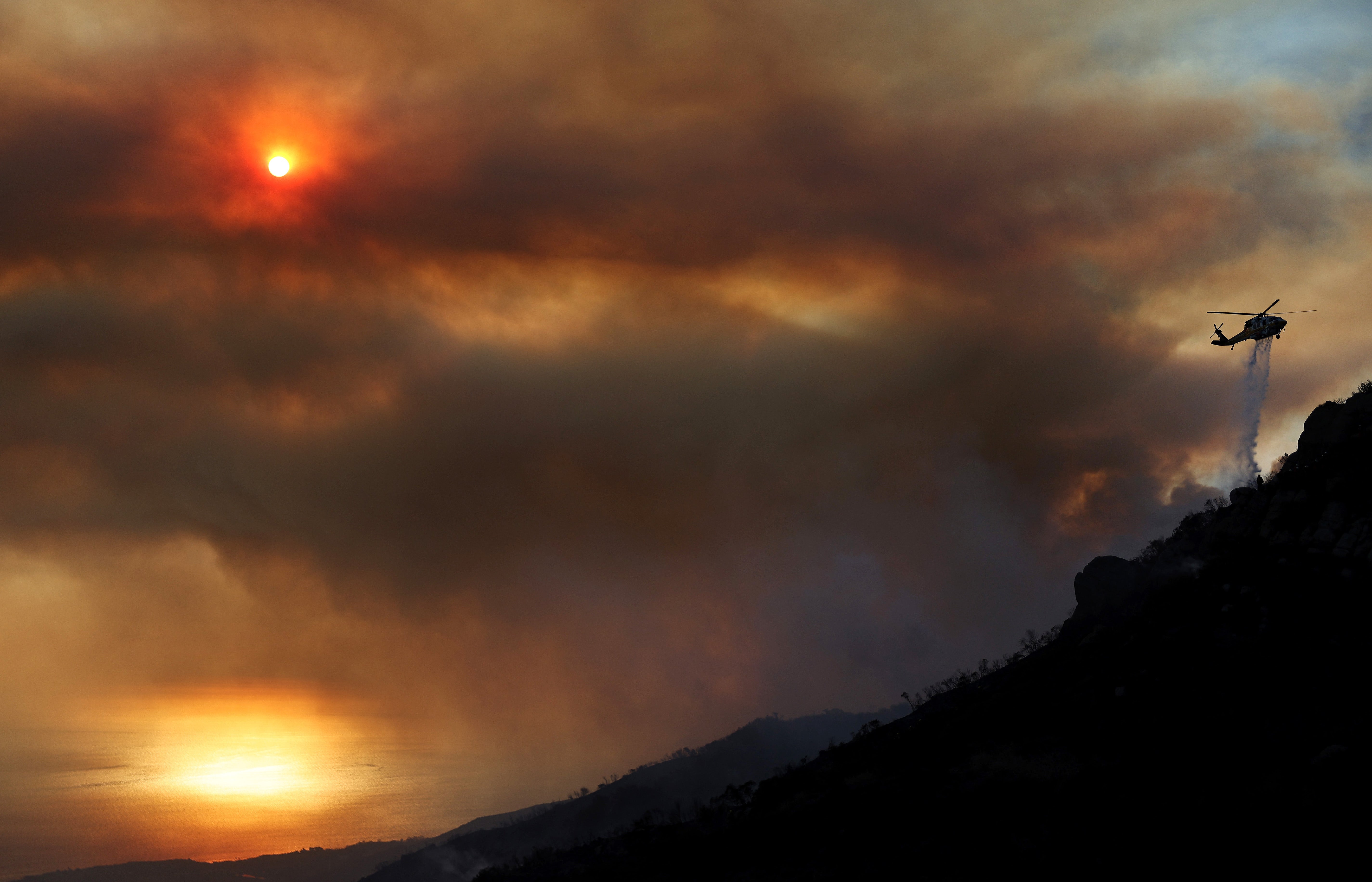 A firefighting helicopter drops water as the Franklin Fire continues to burn