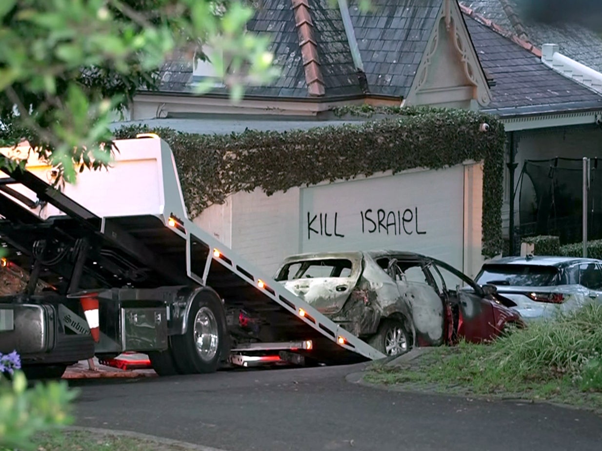 A torched car being removed in front of anti-Israel graffiti written on a wall in the Sydney suburb of Woollahra
