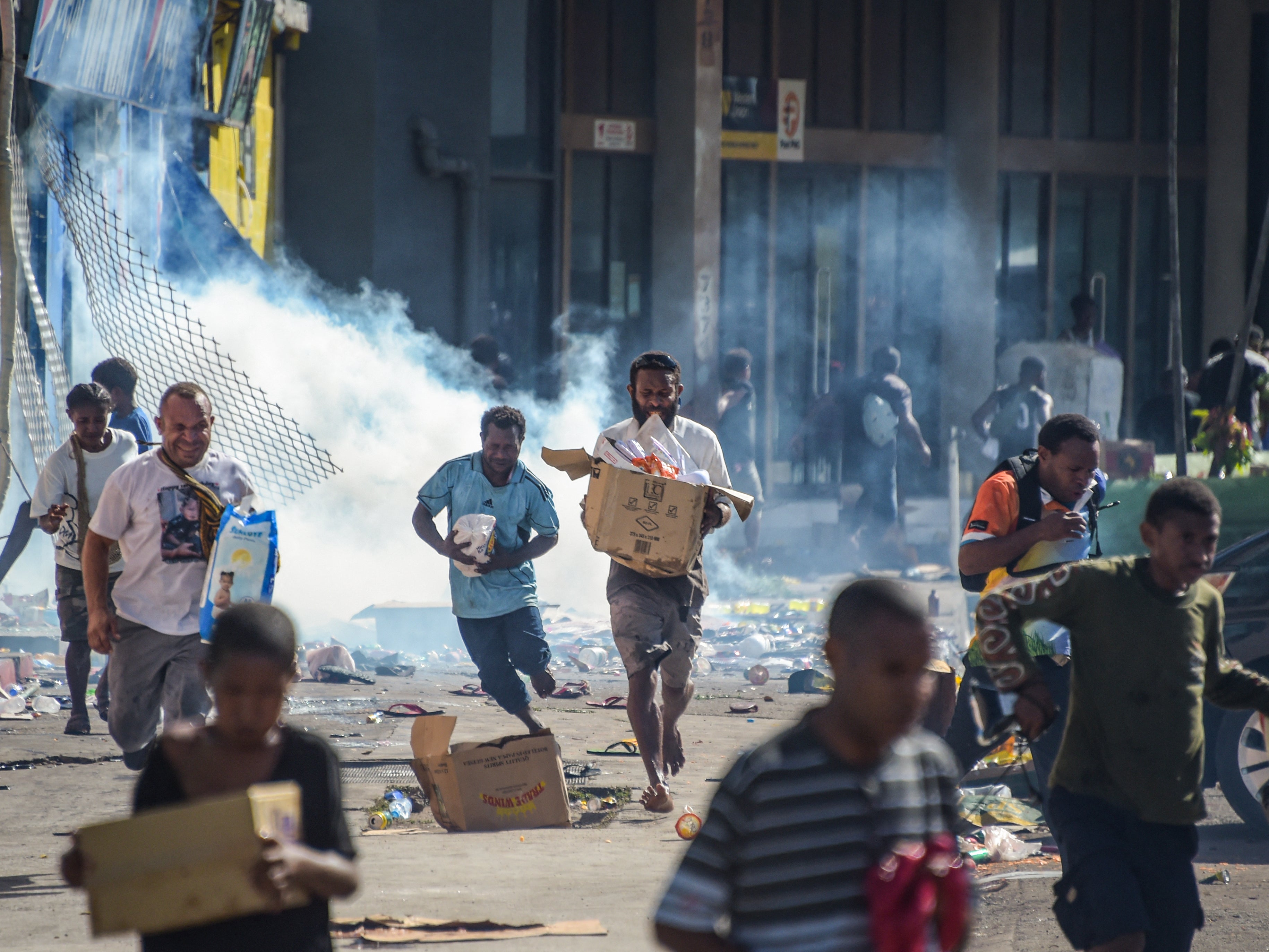 File. People run with merchandise as crowds leave shops with looted goods amid a state of unrest in Port Moresby on 10 January 2024. Following the riots, Papua New Guinea revealed that China had proposed a policing deal