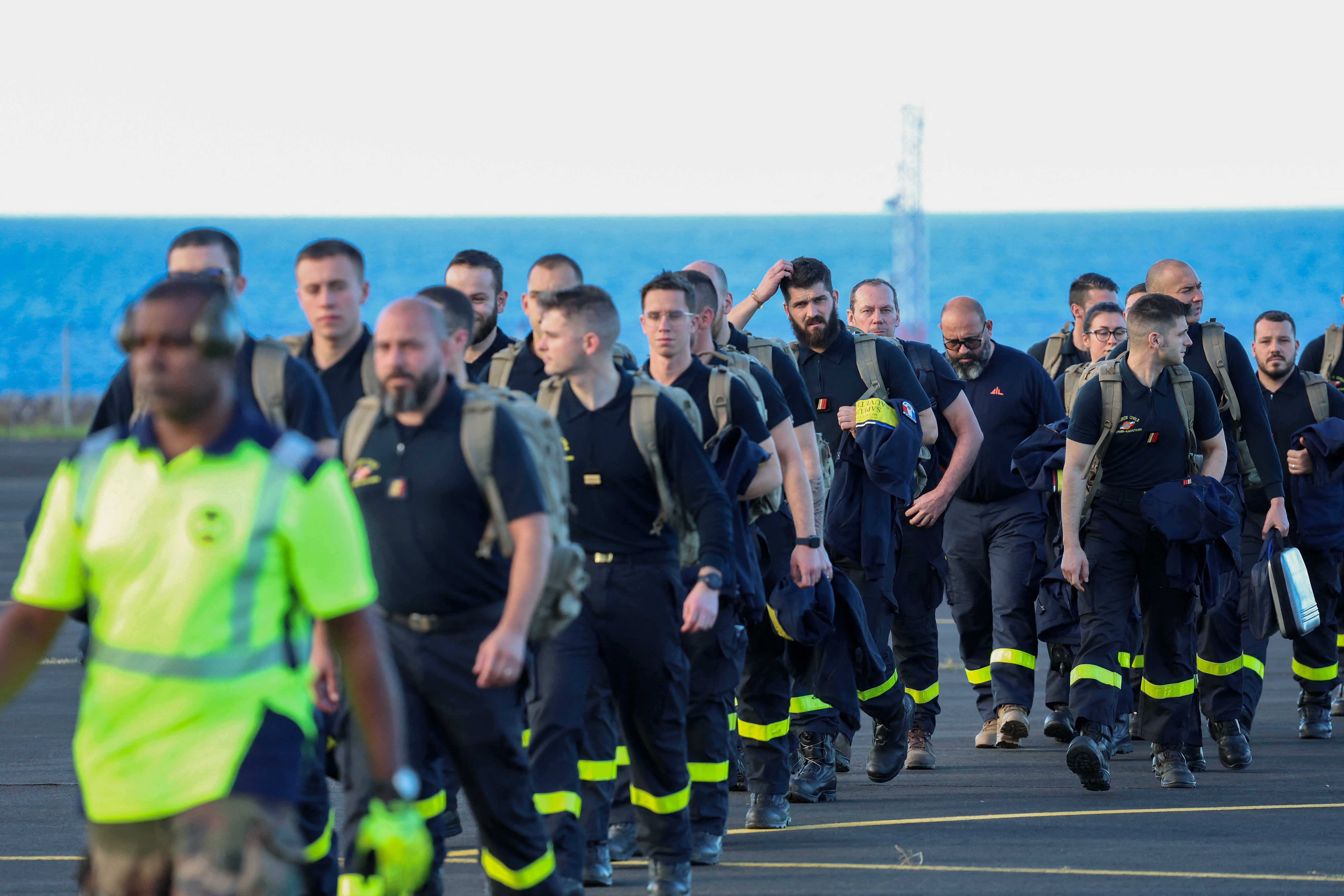 Members of the French Civil protection and French firefighters walk on the tarmac following their landing aboard the A440M military aircraft, as part of an emergency response to bring aid to the small French Indian Ocean territory of Mayotte, almost cut off from the world after the passage of cyclone Chido