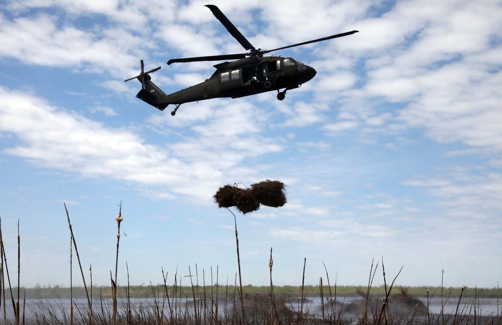 A Louisiana National Guard helicopter carries Christmas trees over the marshland. The marshland helps to protect Louisiana from storms