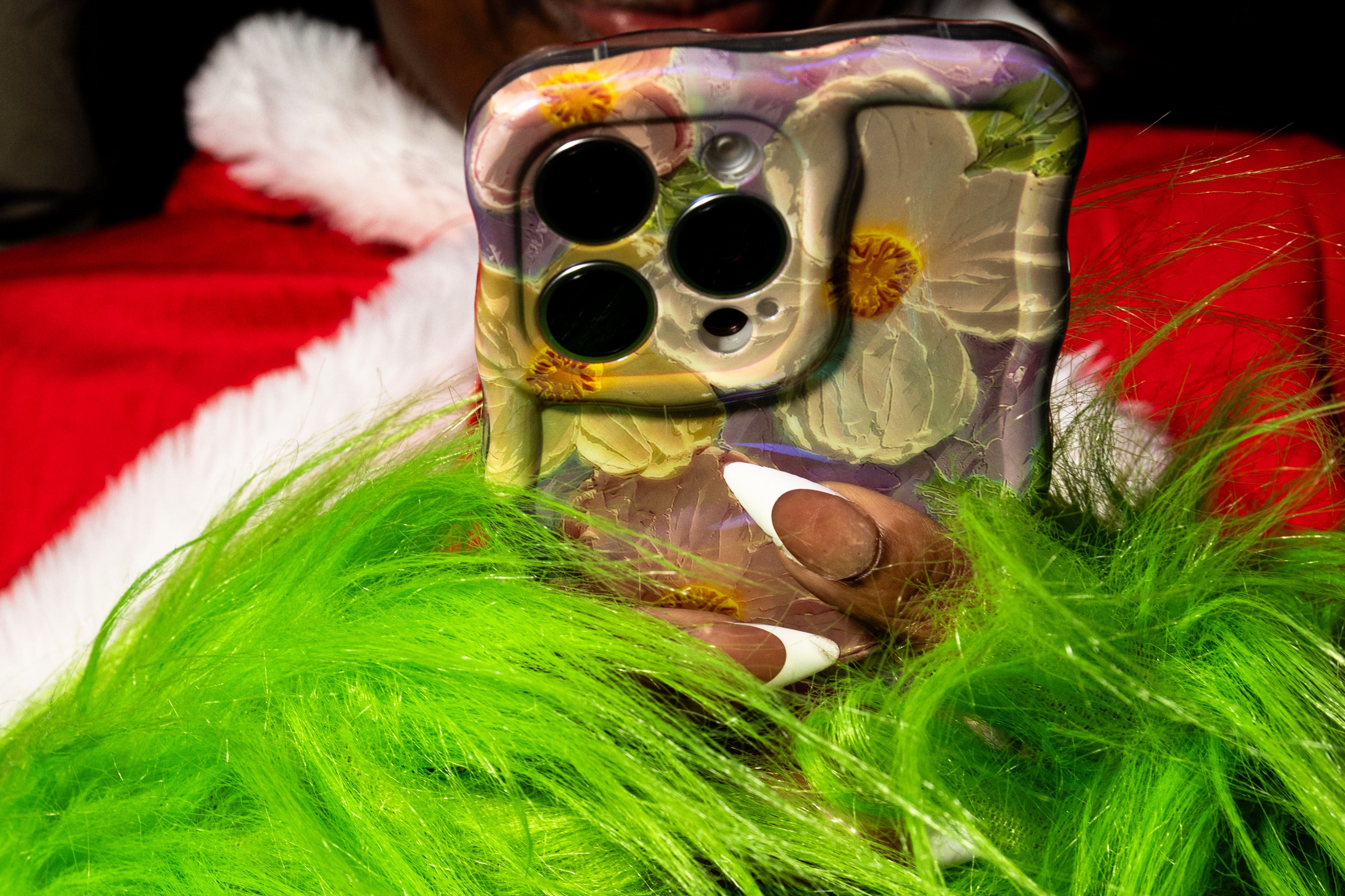 A participant of Santacon wearing Grinch hands texts on her cellphone on 14 December 2024, in New York City