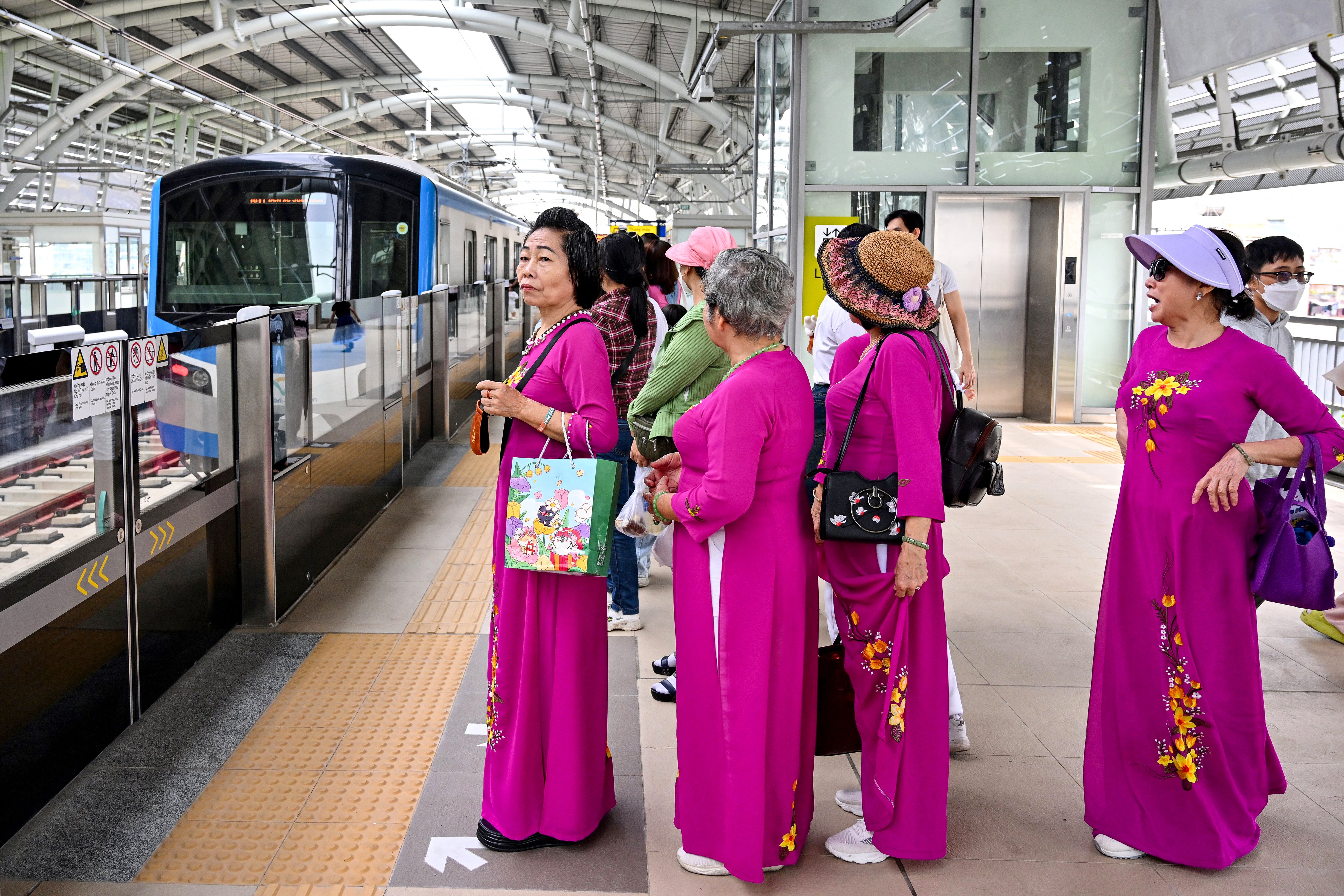 Women in traditional ‘ao dai’ dress wait to board a train