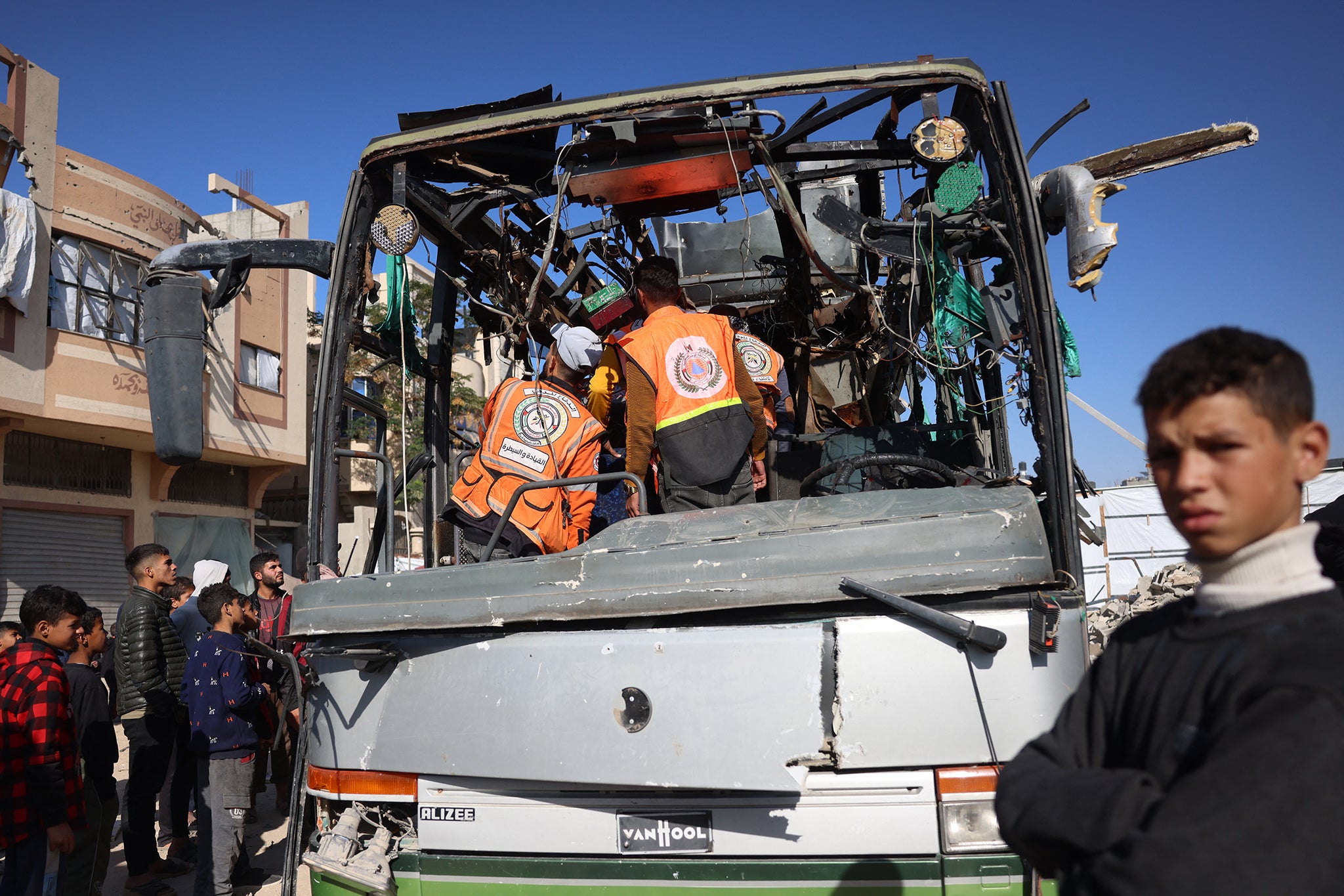 People and rescuers inspect the carcass of a bus hit by an Israeli strike in the Mawasi area of Khan Younis