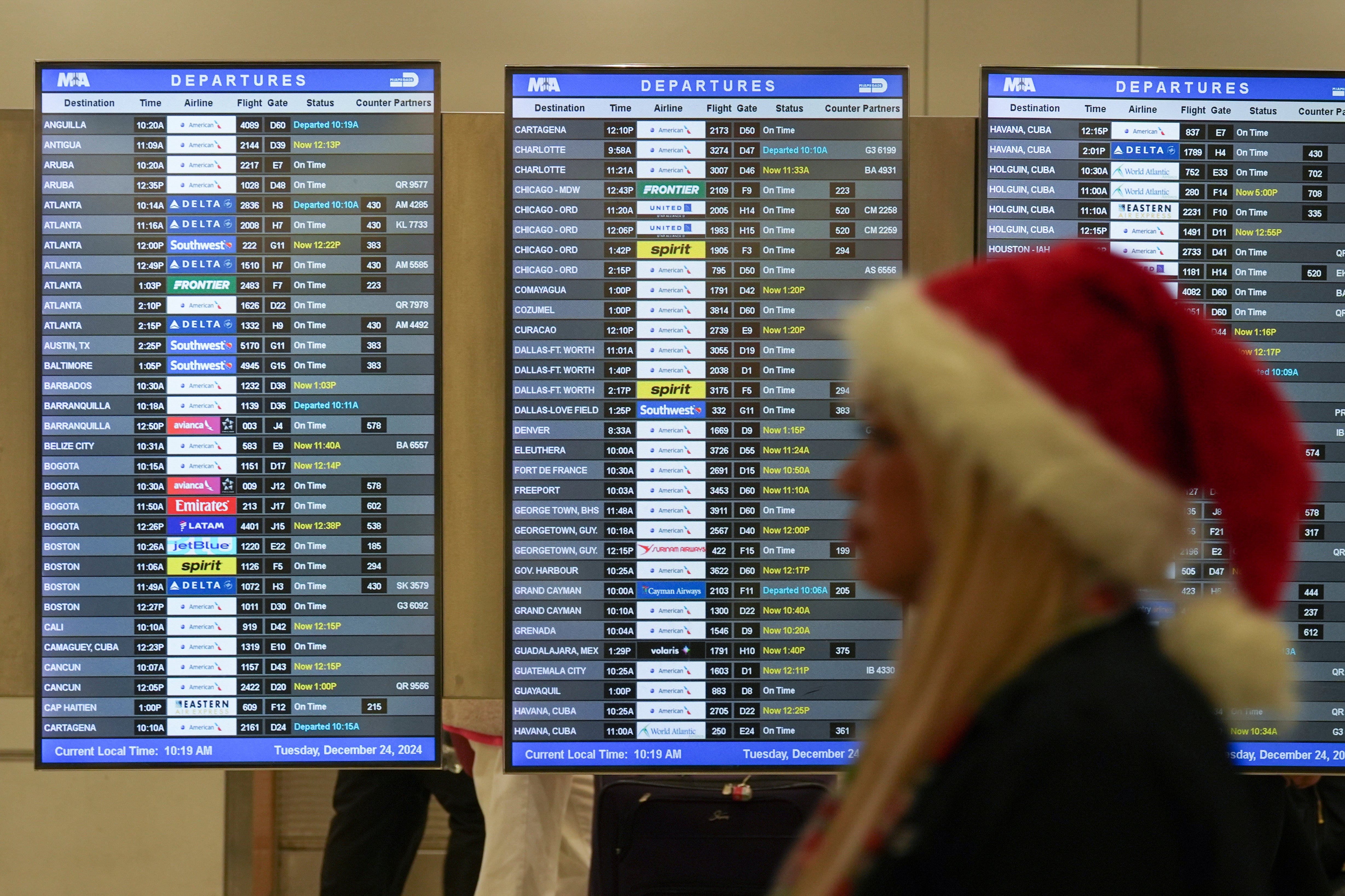 An employee wearing a Santa Claus hat walks past boards showing flight delays, in the American Airlines terminal at Miami International Airport, on Christmas Eve, Tuesday, Dec. 24, 2024, in Miami. (AP Photo/Rebecca Blackwell)