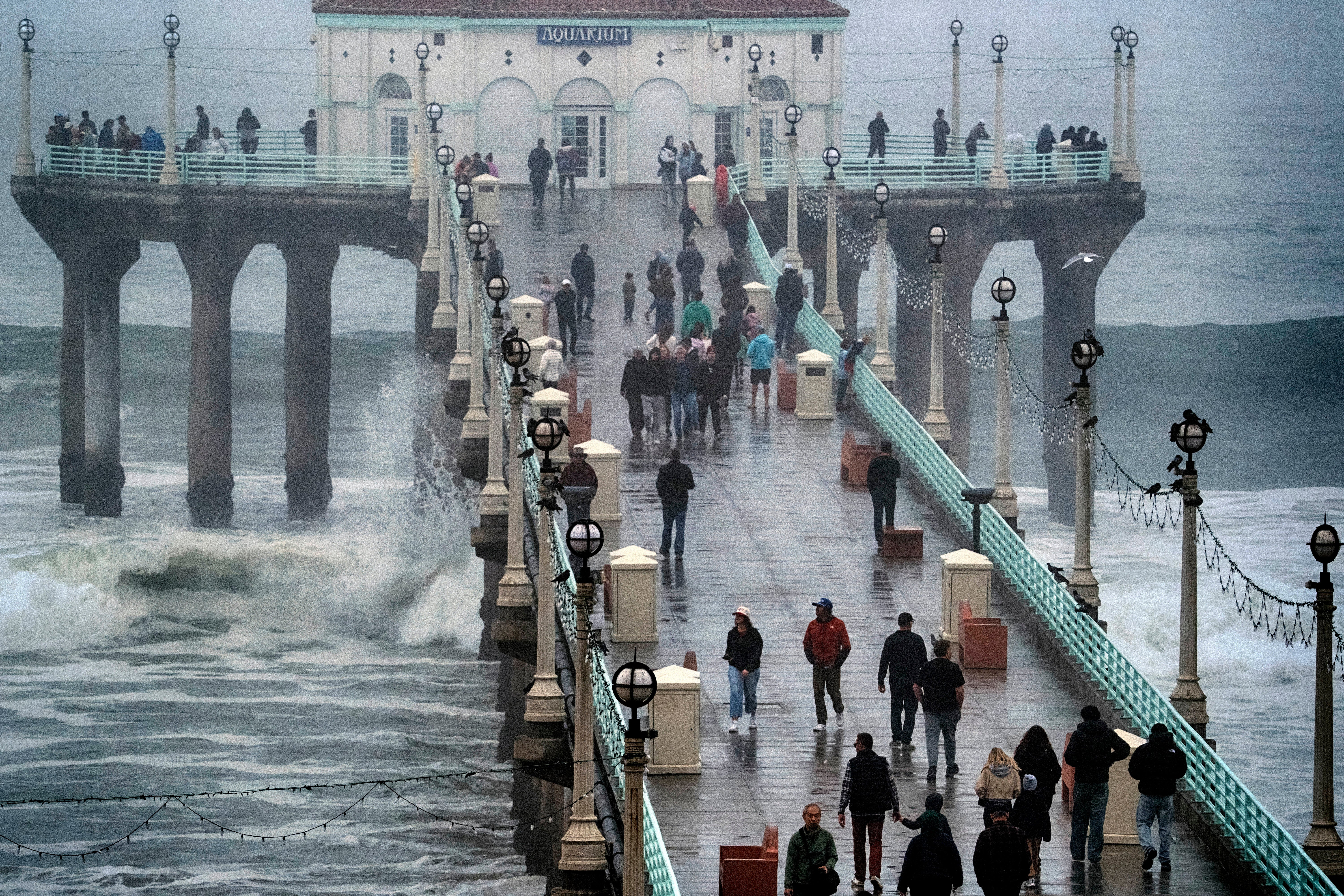 People brave the rain and walk along the Manhattan Beach Pier to watch high surf on Tuesday in Manhattan Beach, California. Damaging winds are forecast to continue near the coast