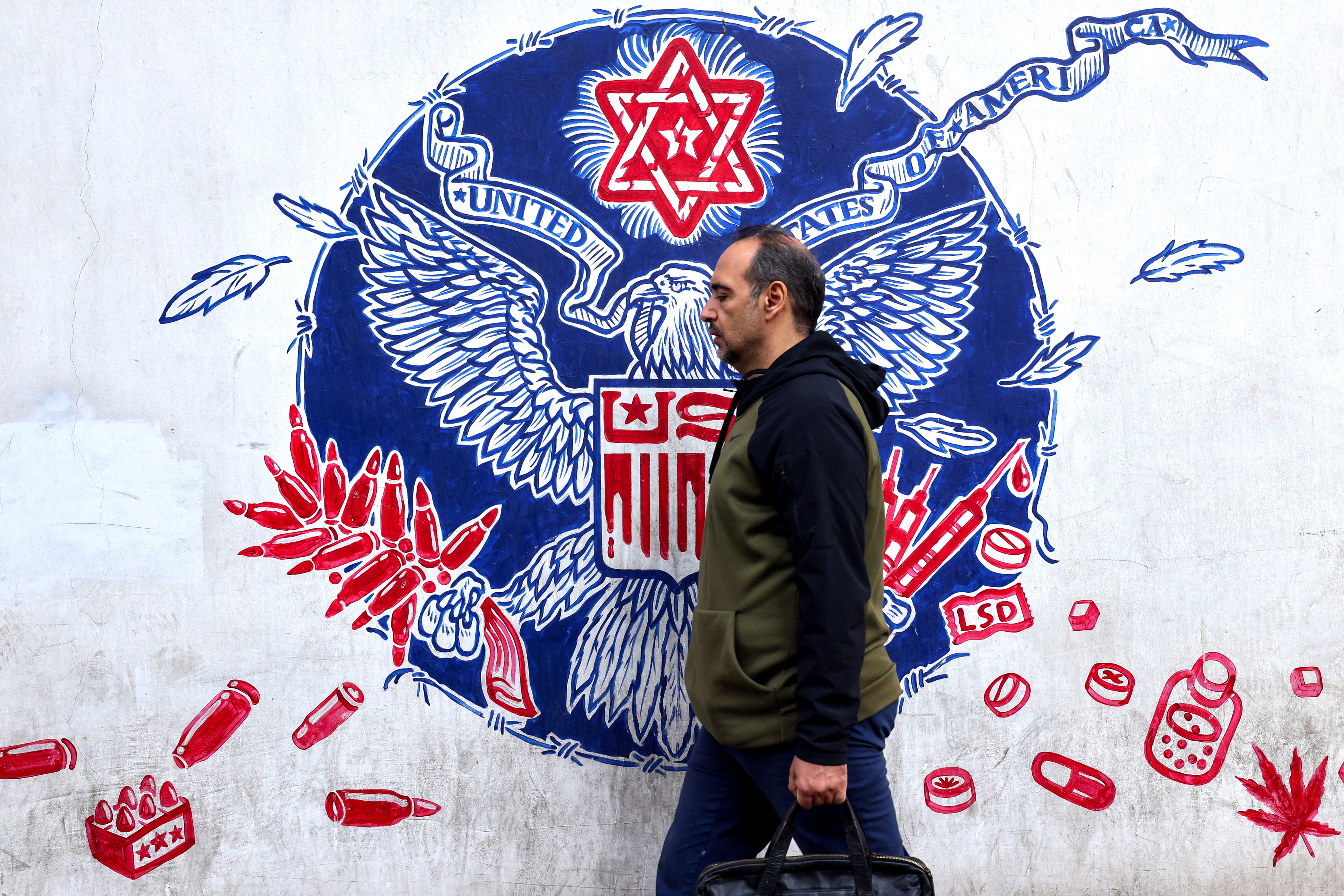 Man walks past a graffiti depicting the Great Seal with a Star of David on top on the walls of the former US embassy in Theran on Monday