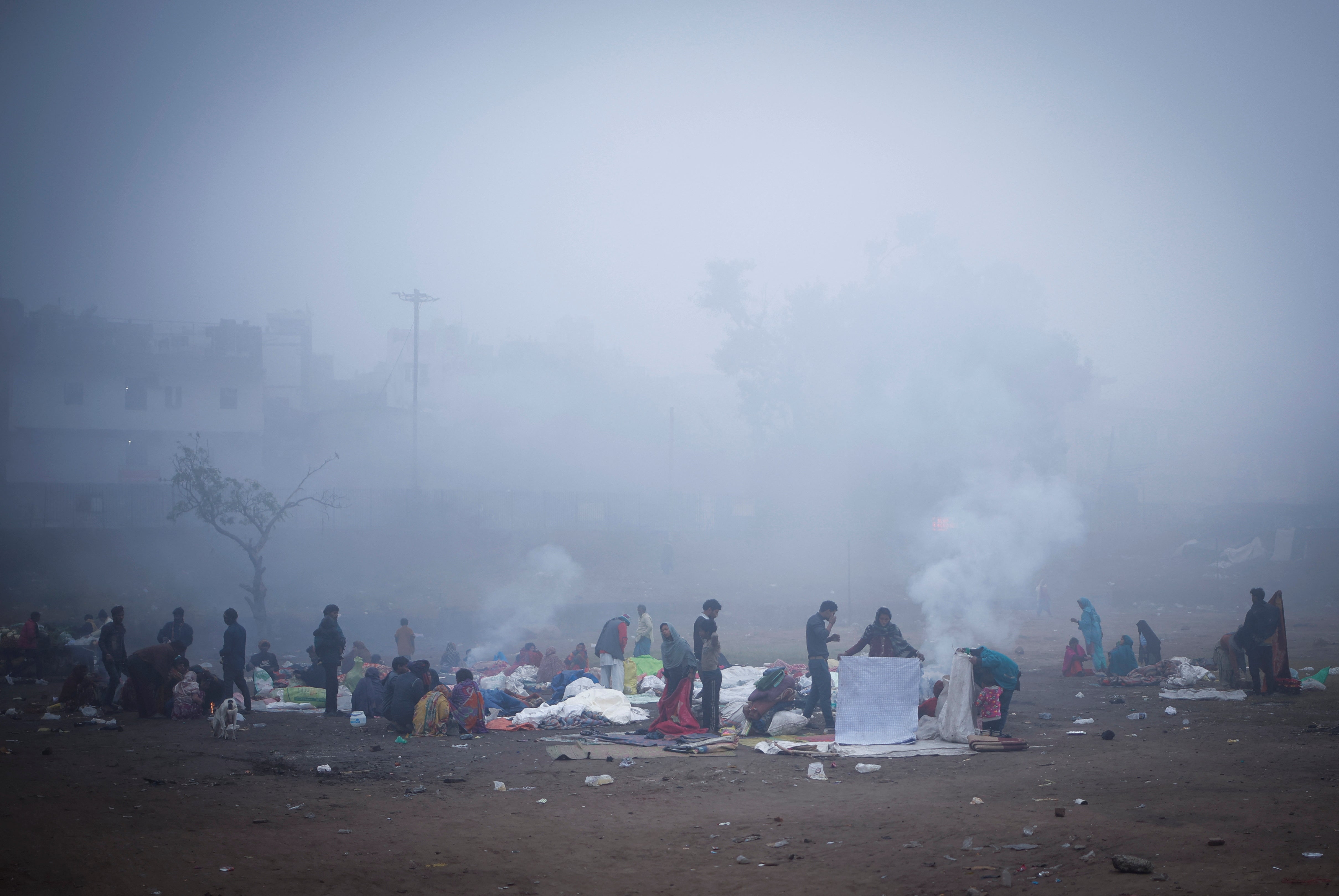 People sit next to a fire at an open ground on a foggy winter morning in the old quarters of Delhi