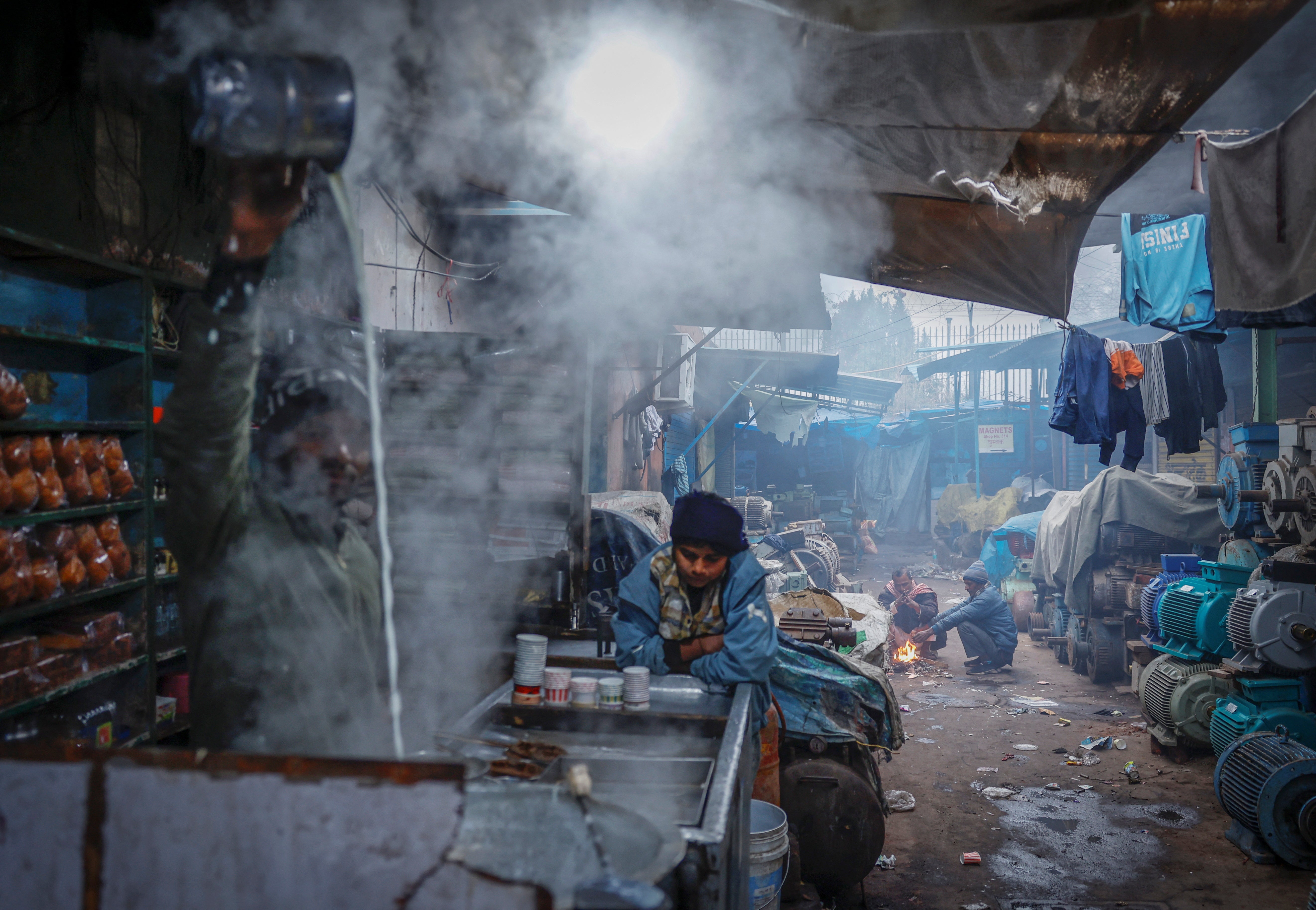 People sit next to a fire at a market area on a cold winter morning in the old quarters of Delhi