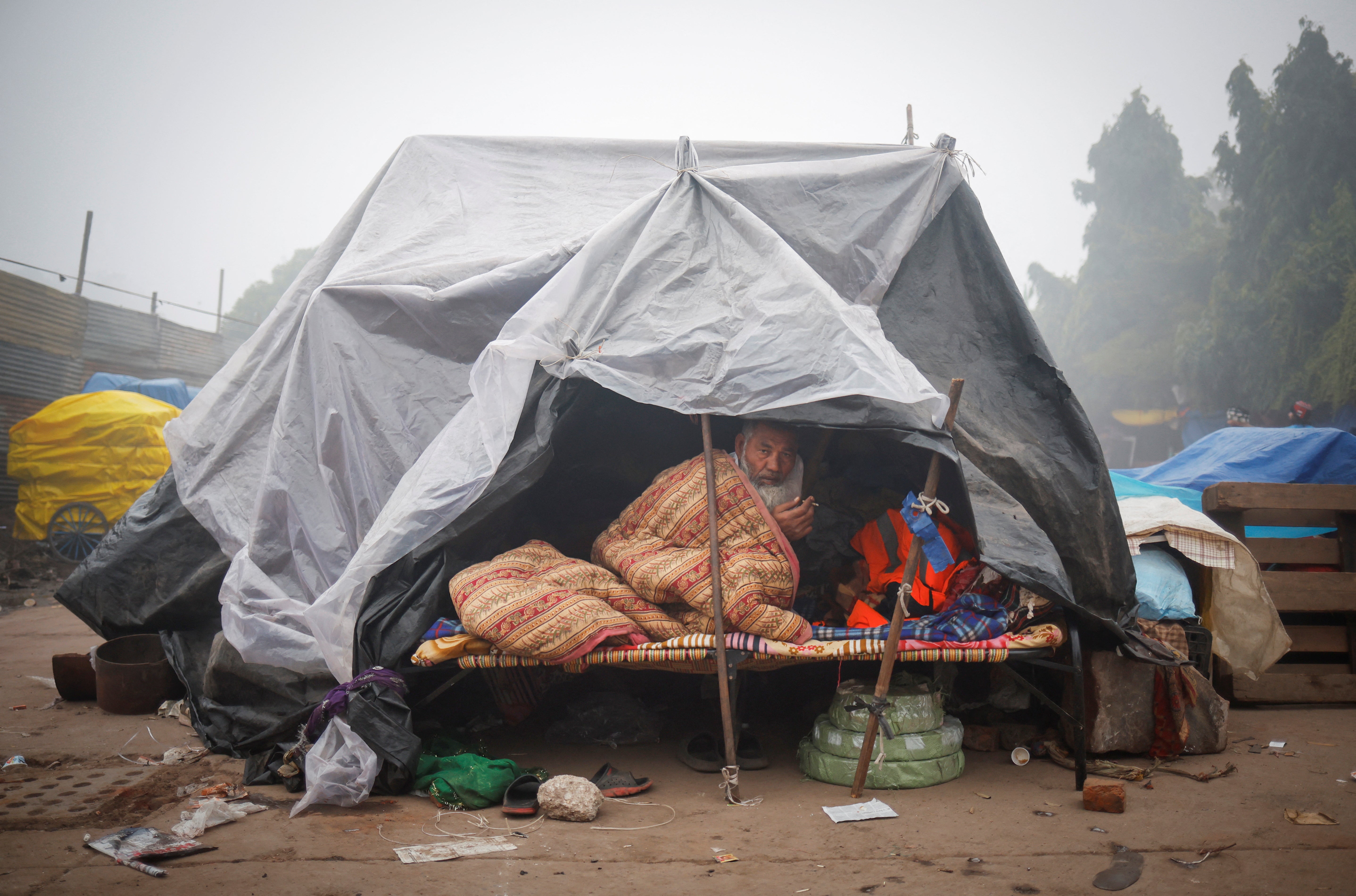 A man wrapped in a blanket sits inside a temporary shelter on a foggy winter morning in the old quarters of Delhi