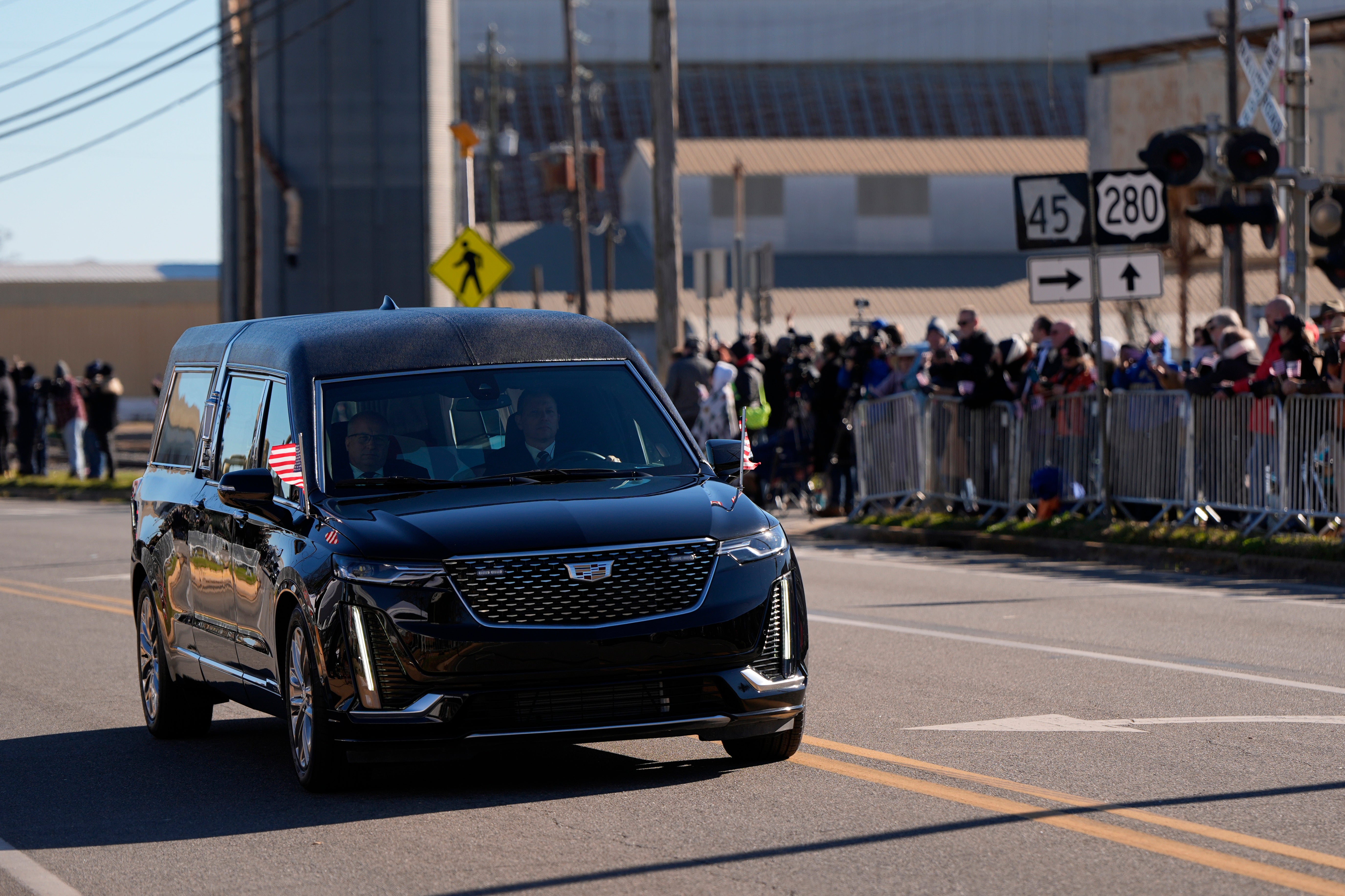 President Jimmy Carter’s hearse drives through Plains, Georgia as people gather to mourn the 39th president