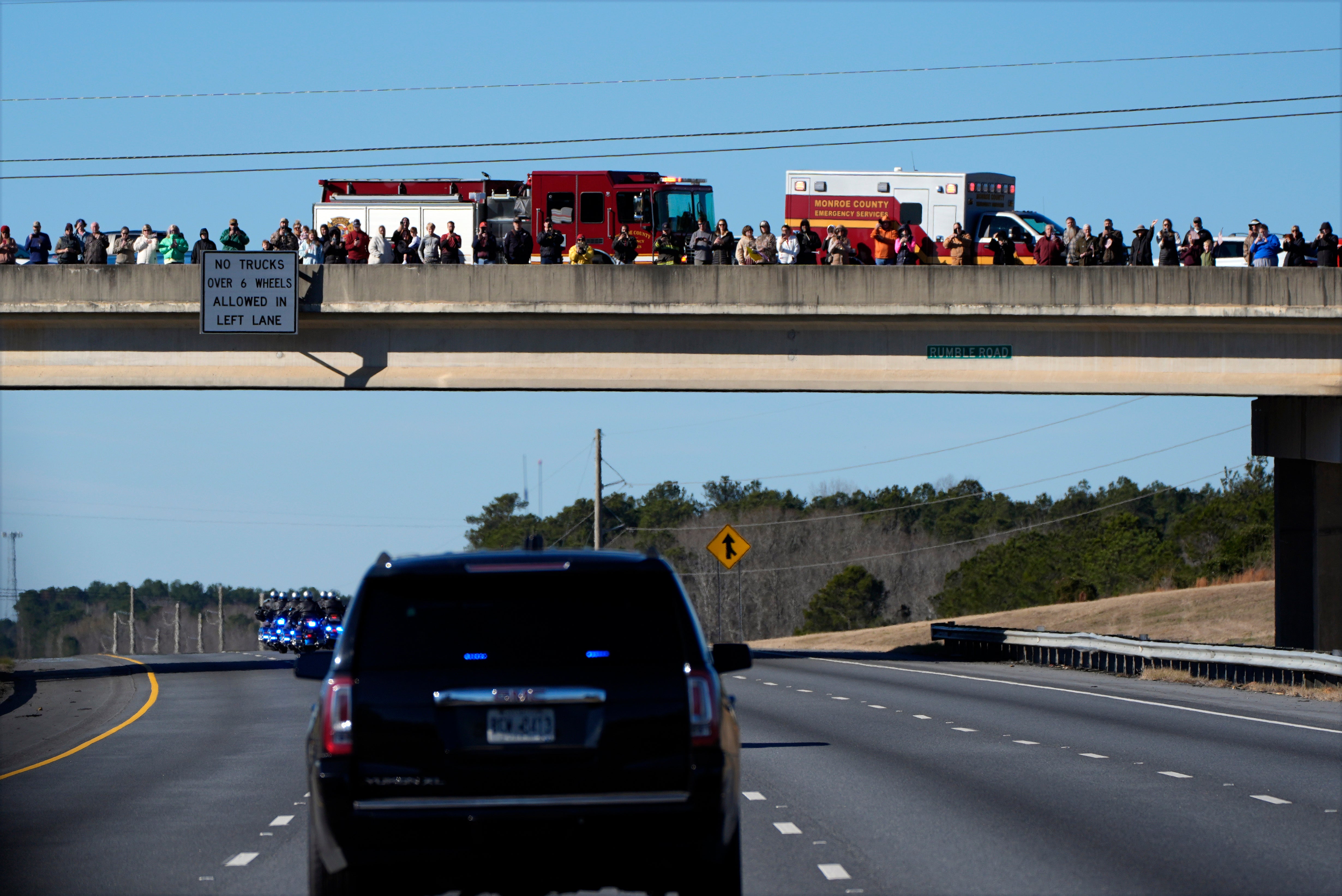 Mourners gather on an overpass to watch former president Jimmy Carter’s casket drive on I-75 toward Atlanta, Georgia