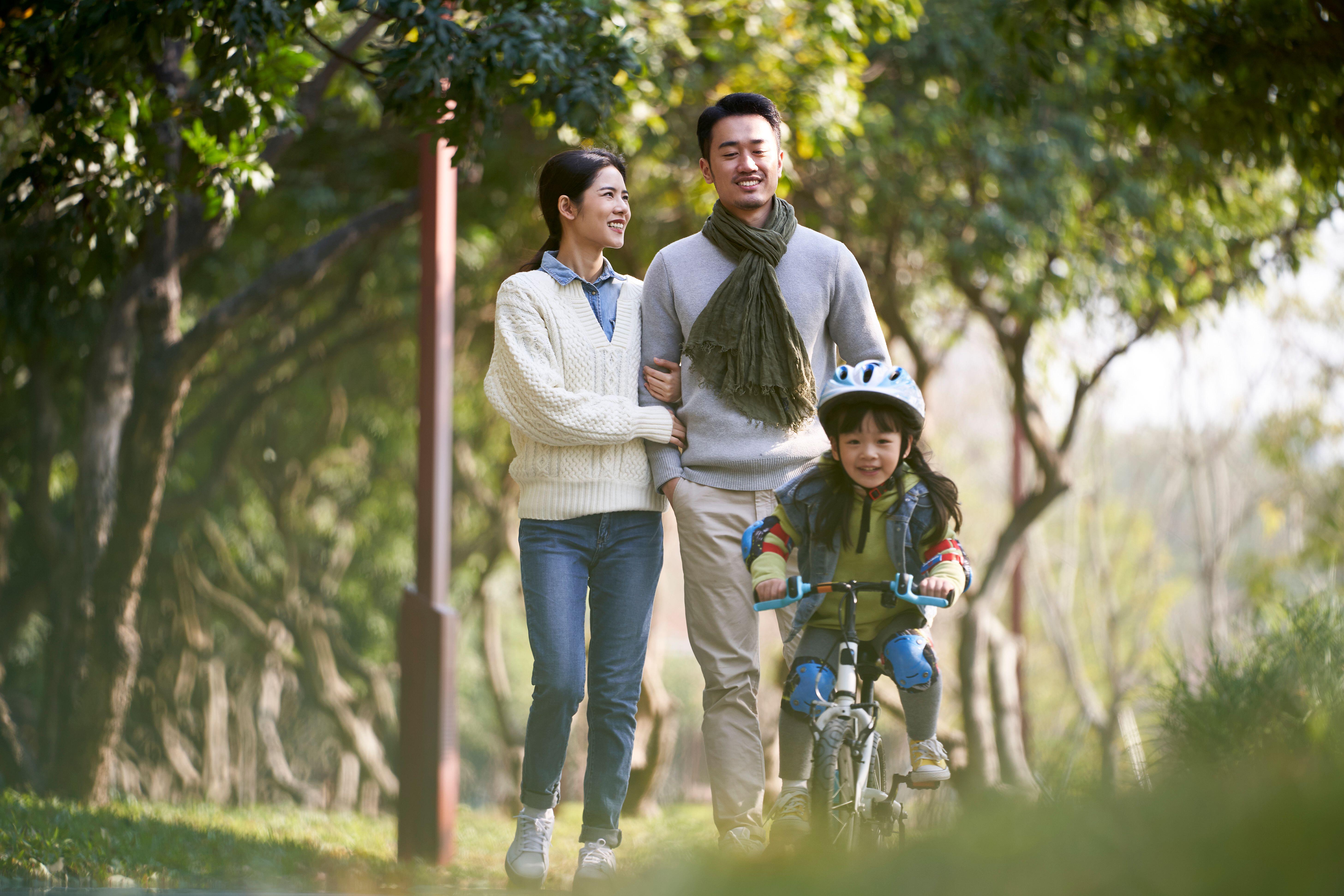 Young man and woman enjoying a walk in a park while their daughters rides on a bike infront of them