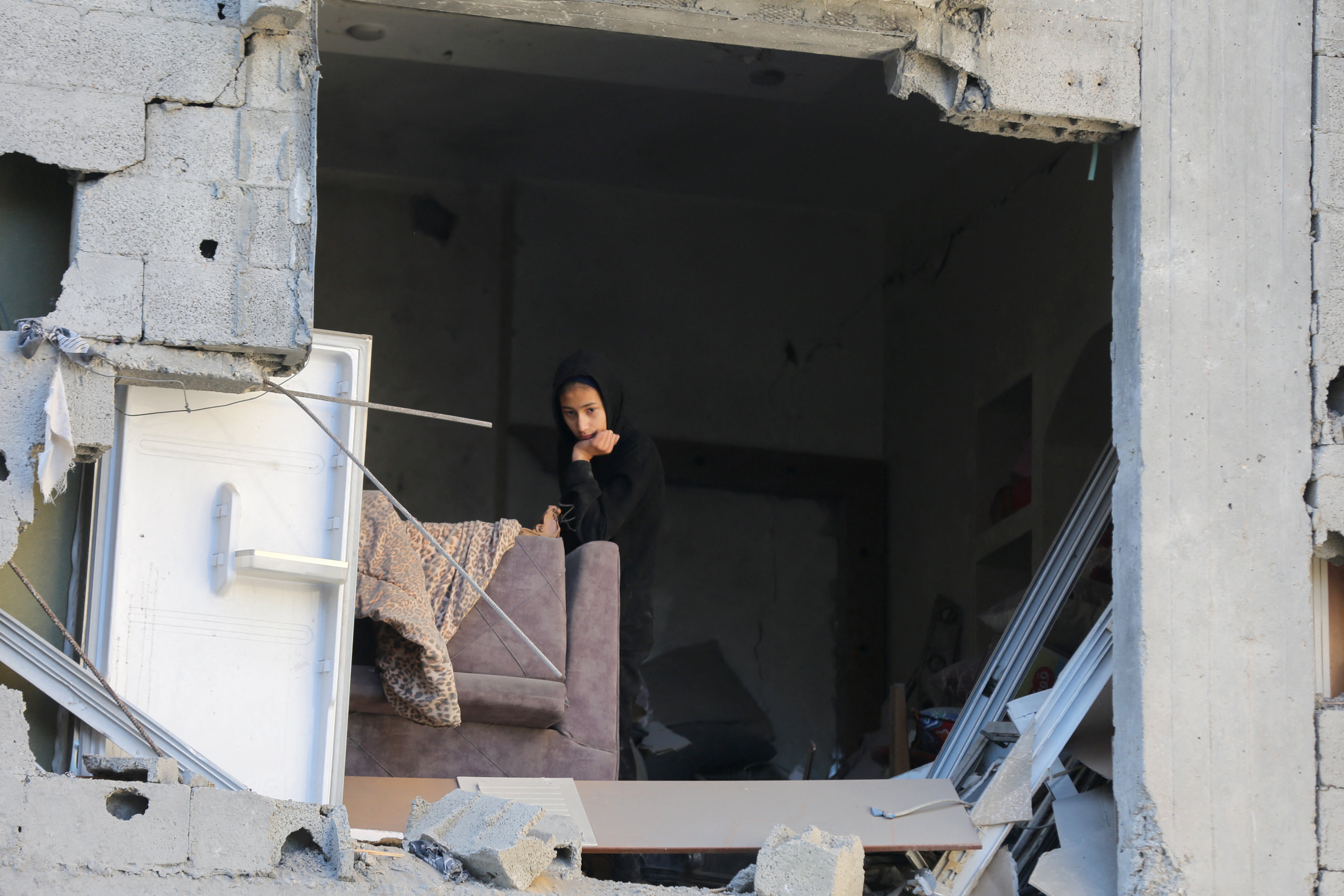 A girl rests on a sofa as she looks out at damaged caused by Israeli airstrikes on Gaza