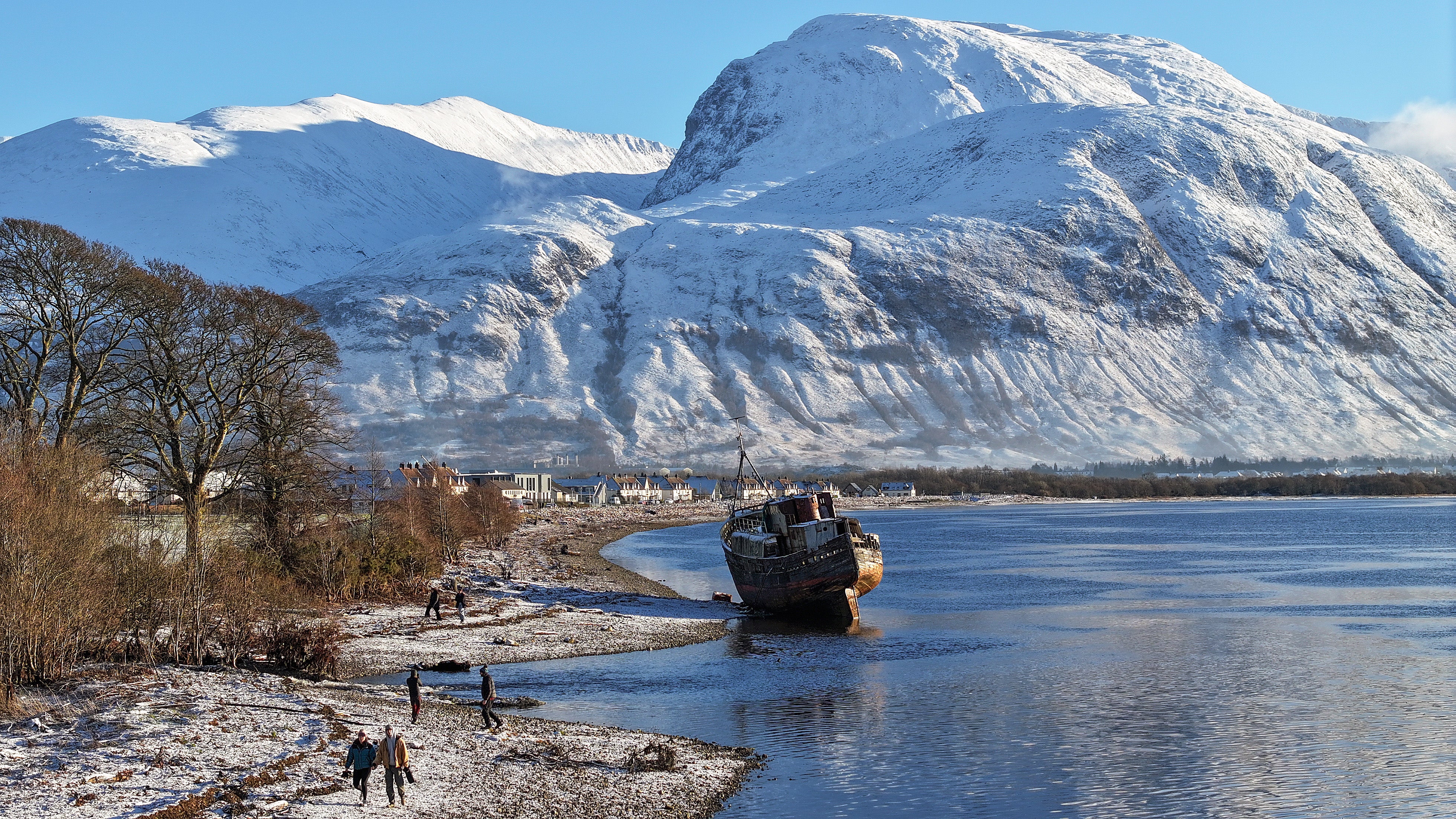 People view a former fishing boat covered in snow on the shore of Loch Linnhe in front of Ben Nevis