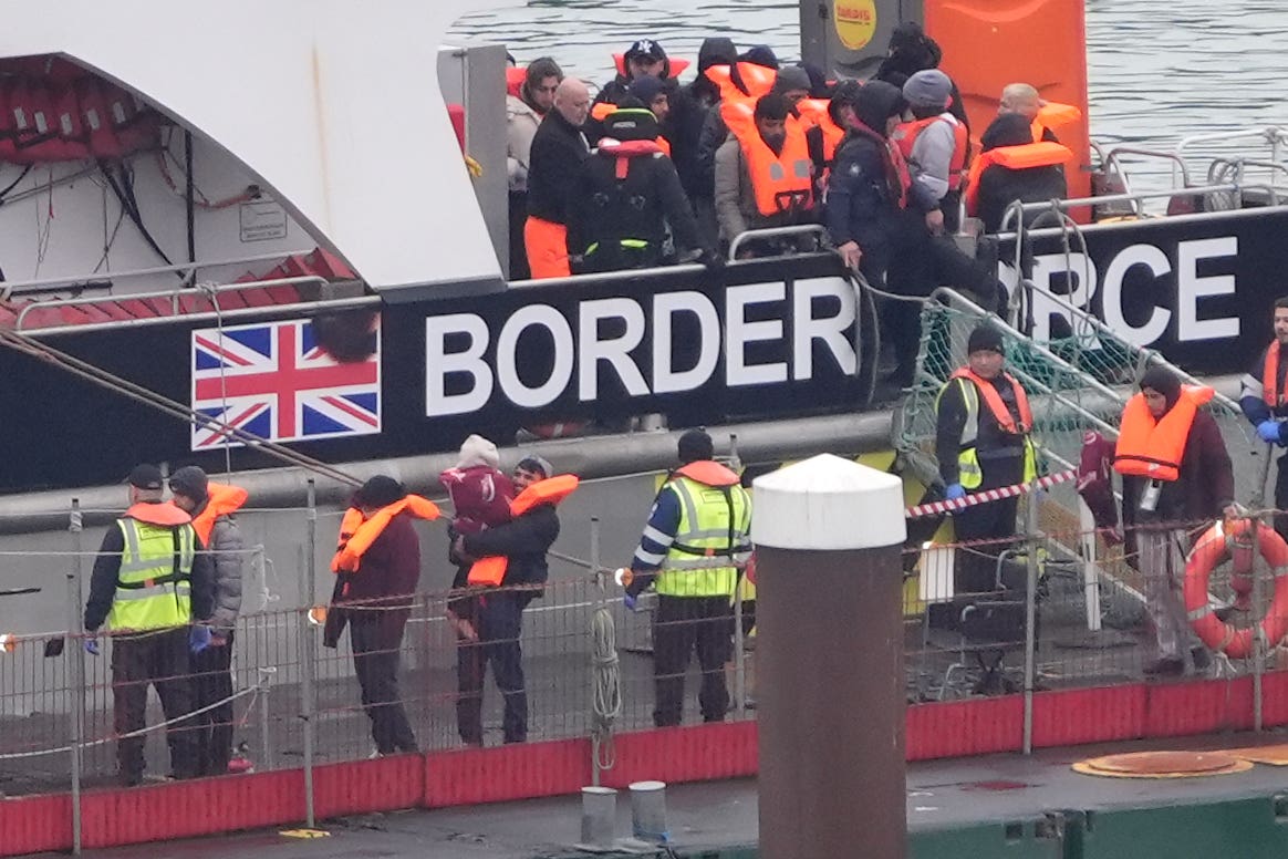 A man carries a young child as a group of people thought to be migrants are brought in to Dover (PA)