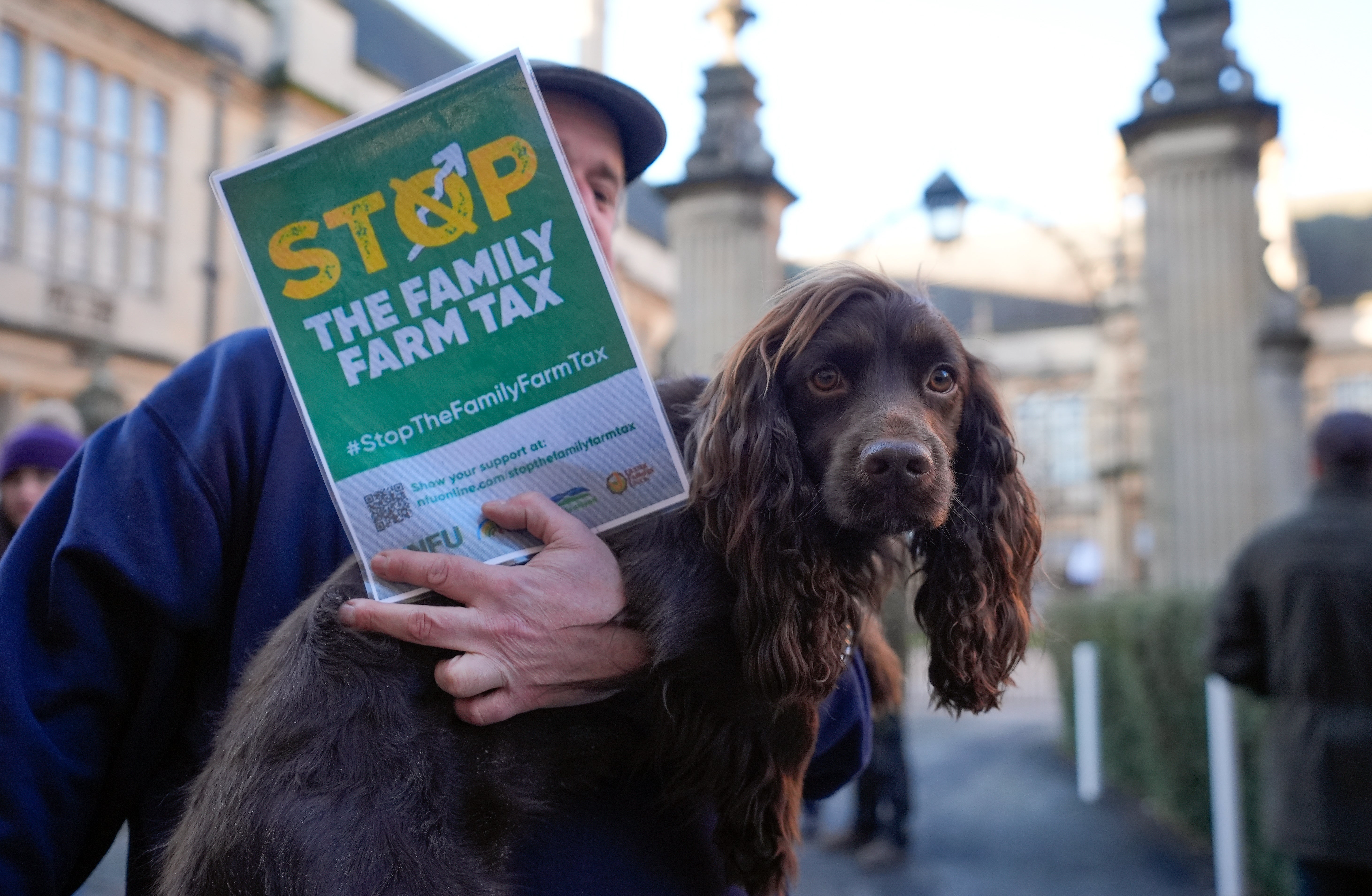 A farmer holds his dog as he takes part in a protest over the changes to inheritance tax rules outside the Oxford Farming Conference (Andrew Matthews/PA)