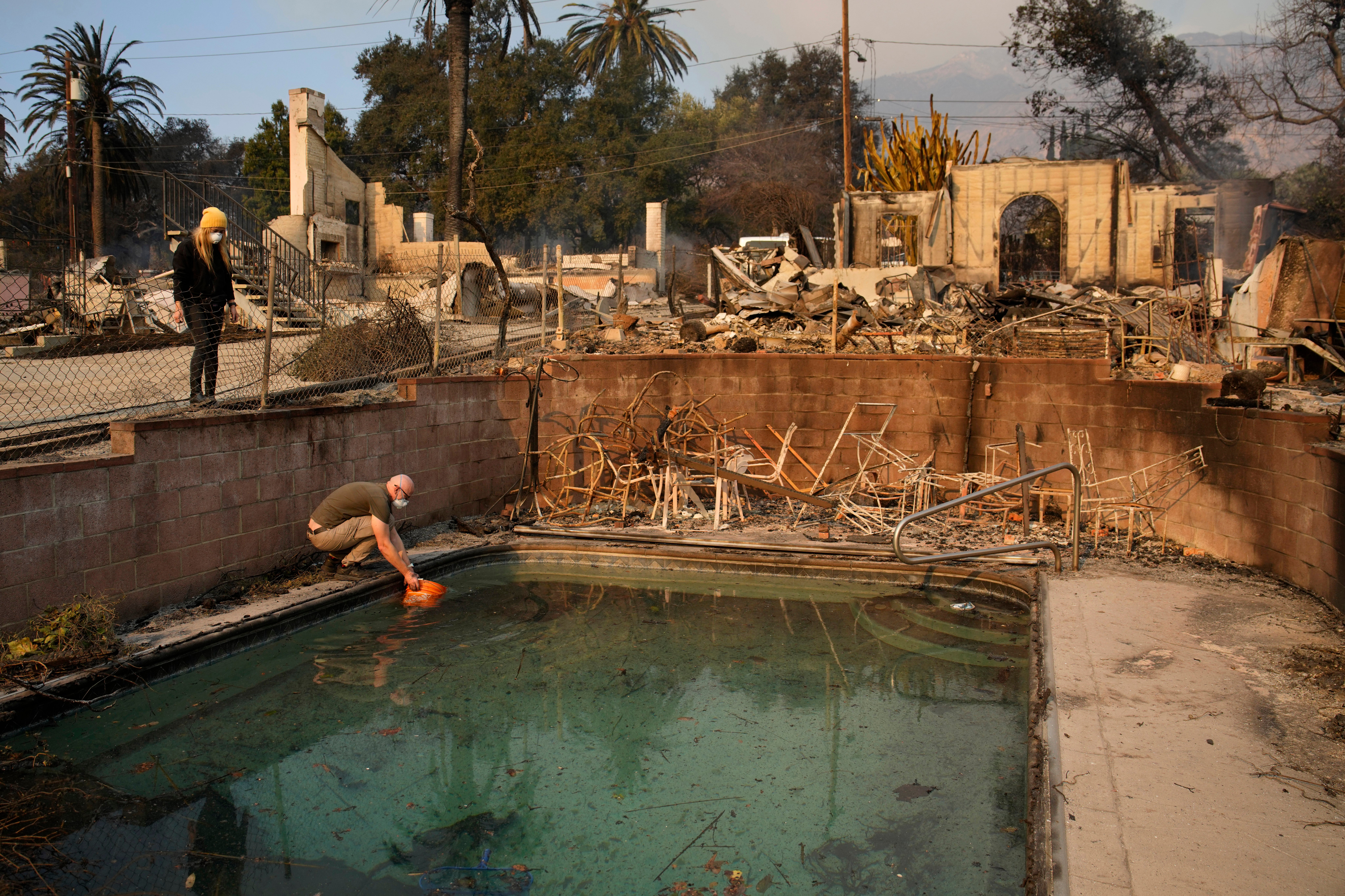 Robert Karban fills a bucket with water from a swimming pool to put out hot spots at a home destroyed by the Eaton fire,.