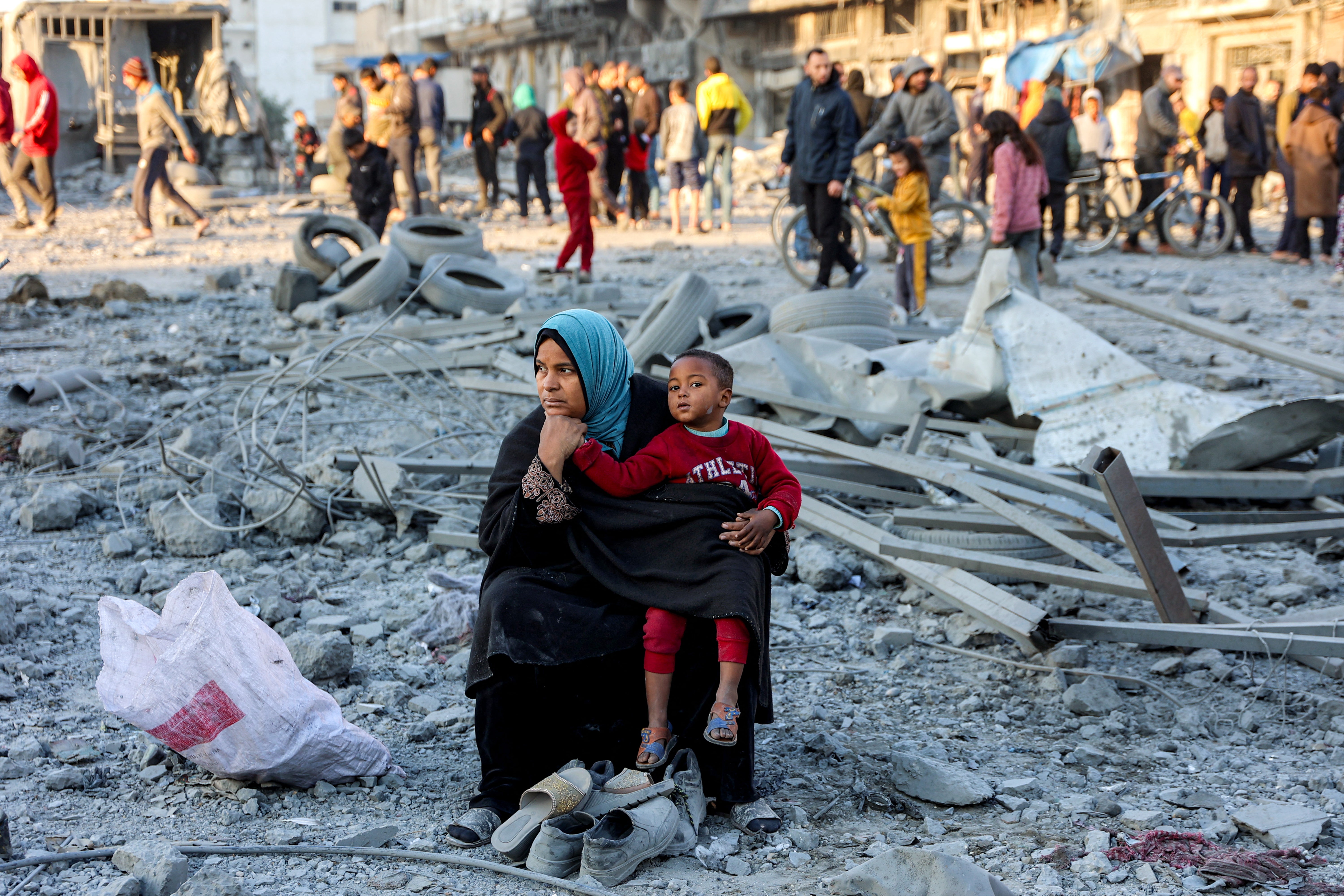 A woman sits with a child with salvaged footwear at the site of an Israeli bombardment in Gaza City