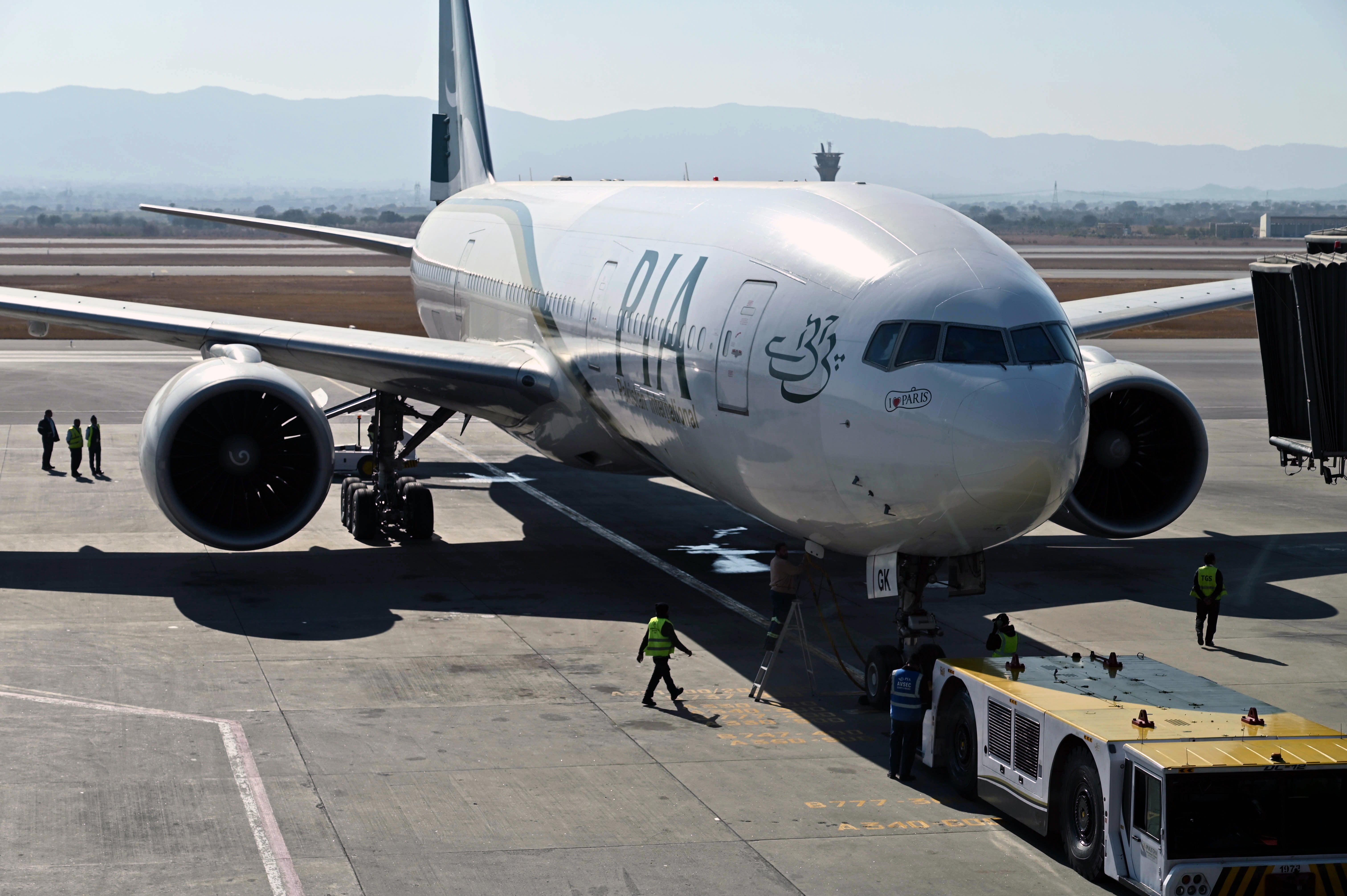 Ground staff stand next to the Pakistan International Airline aircraft ahead of its takeoff for Paris at the Islamabad International Airport