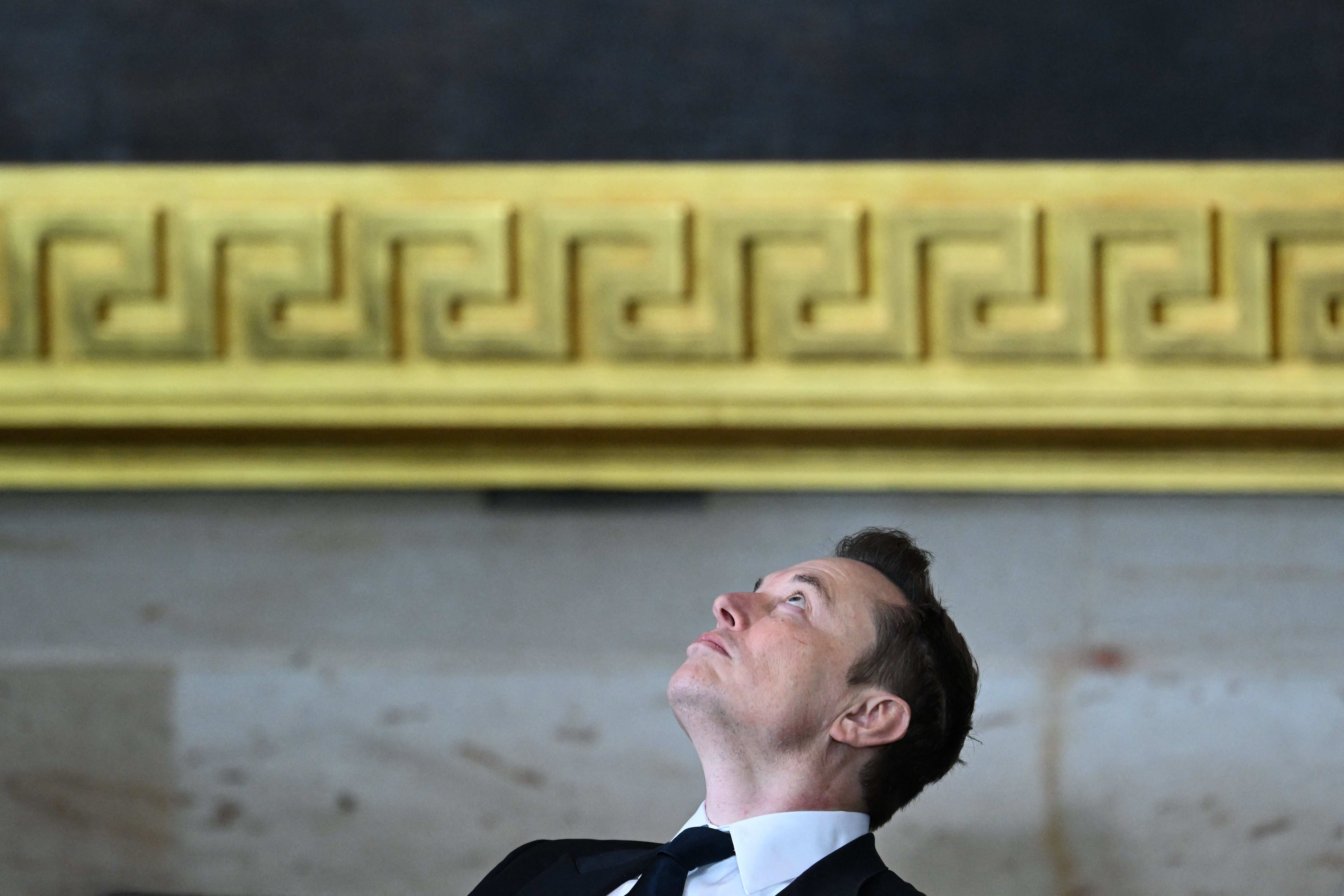 Tesla and SpaceX CEO Elon Musk looks upward as he sits during the inauguration