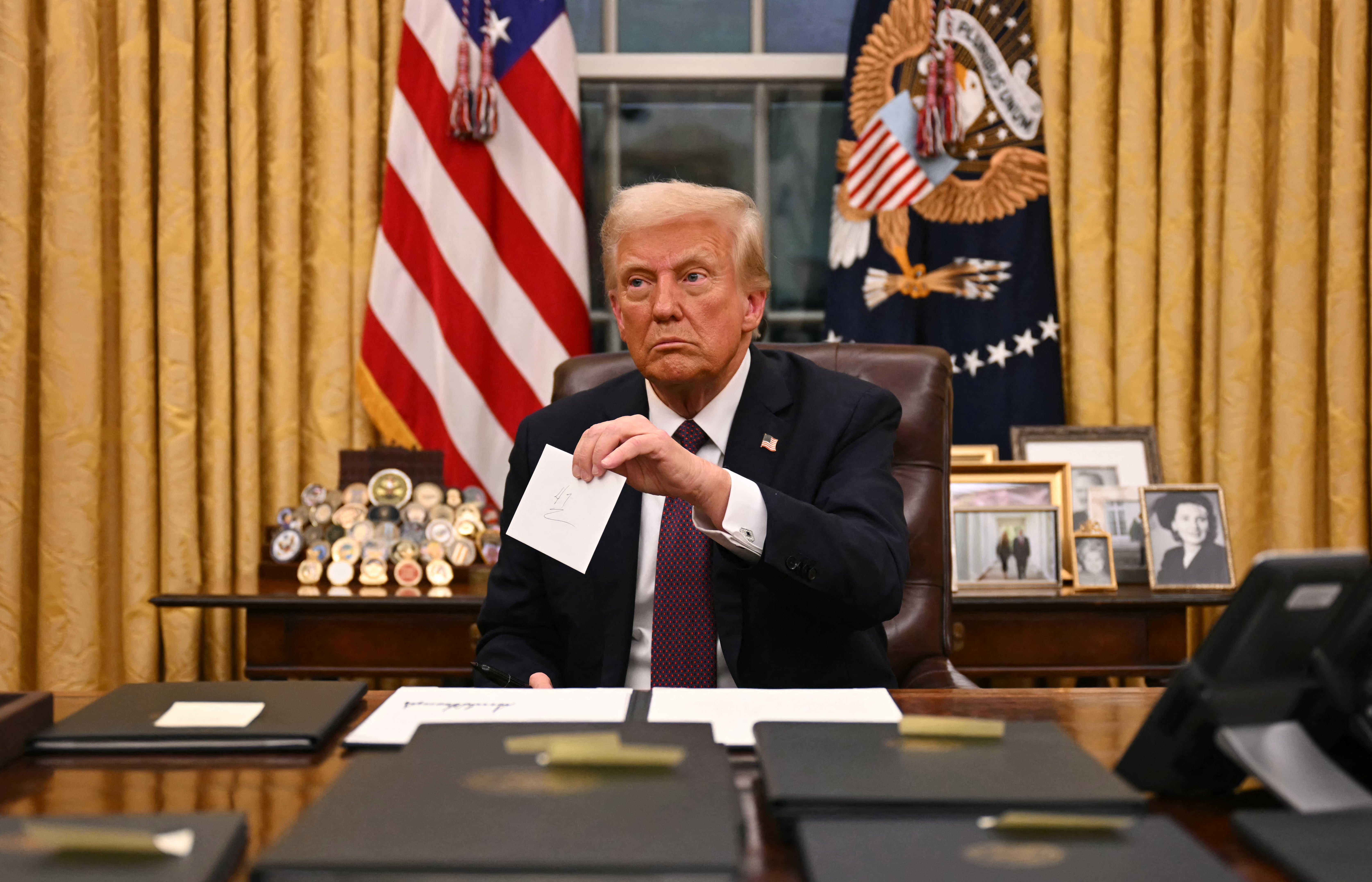 President Donald Trump holds up outgoing president Joe Biden’s letter as he signs executive orders in the Oval Office - one labeled drug cartels as terrorists organizations