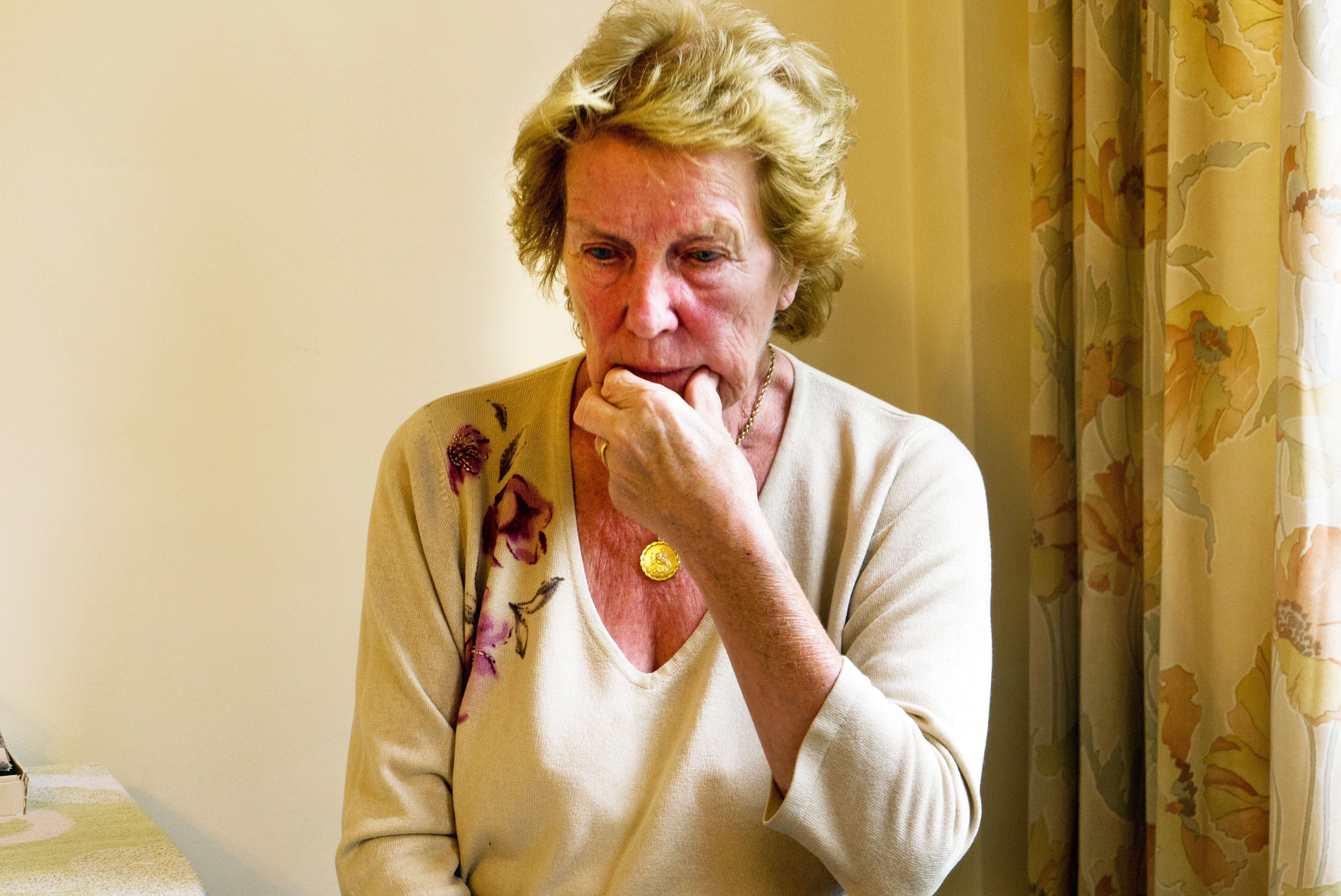An elderly woman with Dementia and Alzheimer’s Disease sitting in her home looking confused and worried.