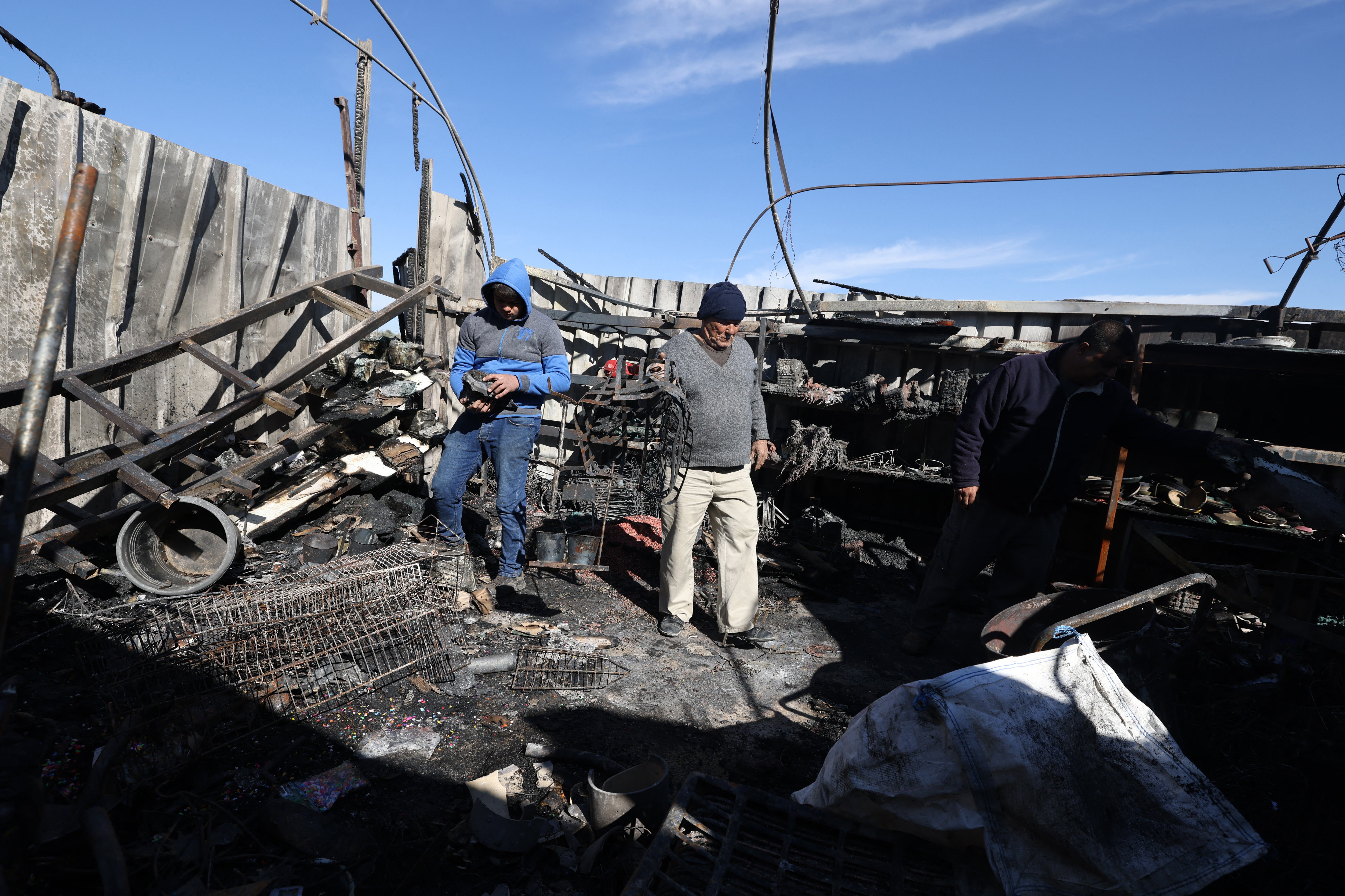 Men check burnt structures following an attack by Israeli settlers in the Palestinian village of Jinsafut