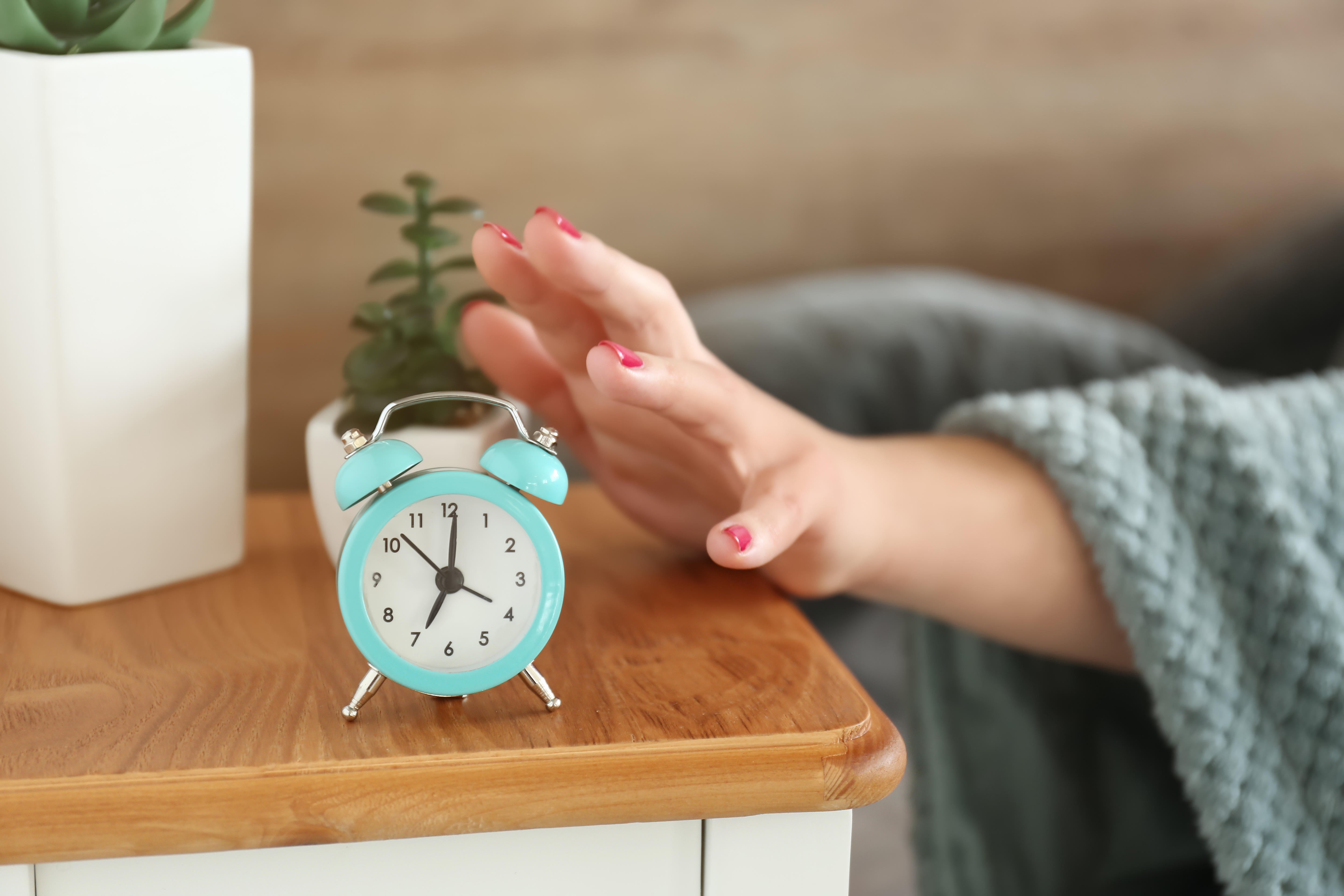 A woman’s hand emerging from under a duvet to turn off an alarm clock (Alamy/PA)