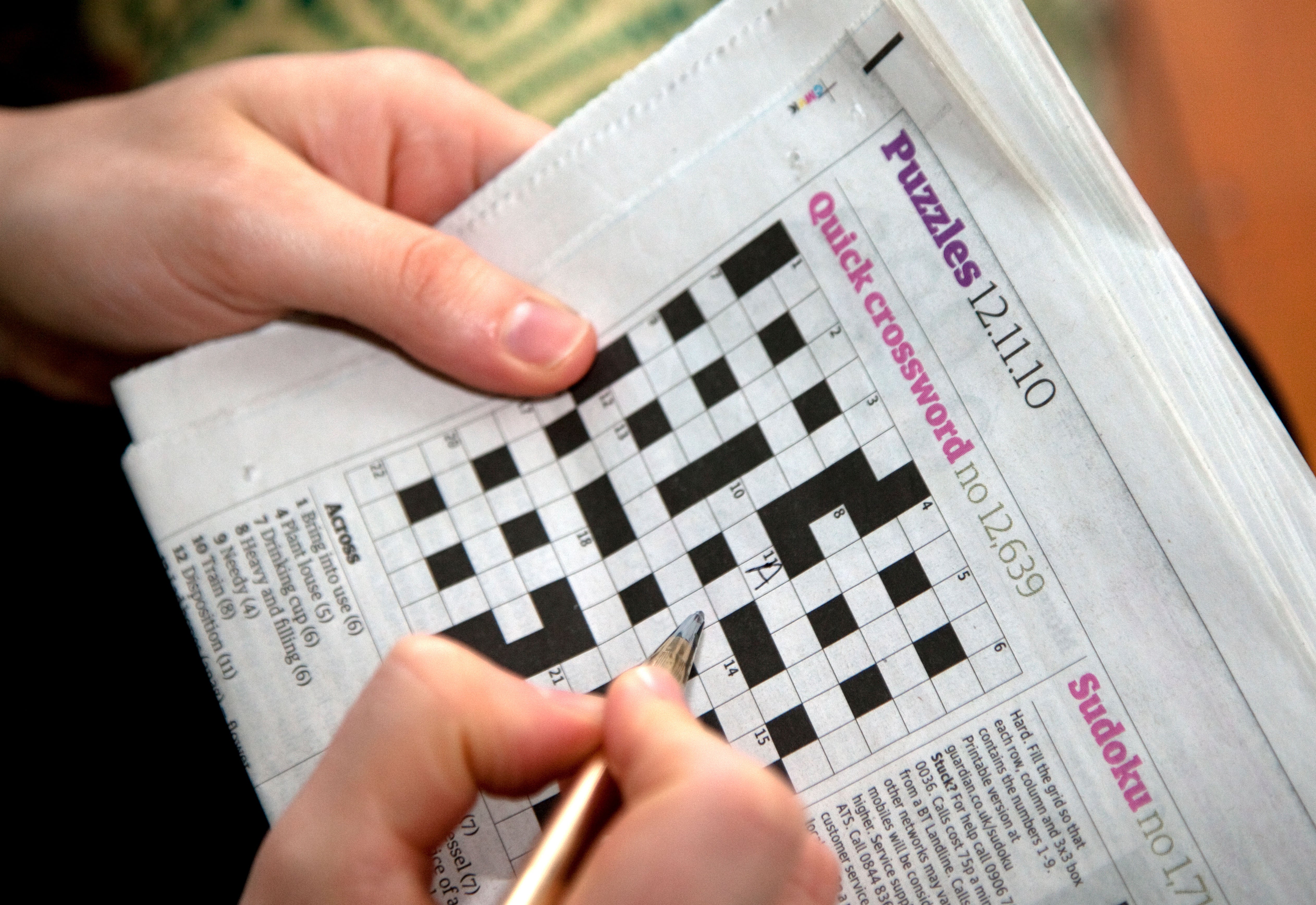 Picture of a woman filling in answers to a crossword in a newspaper (Alamy/PA)