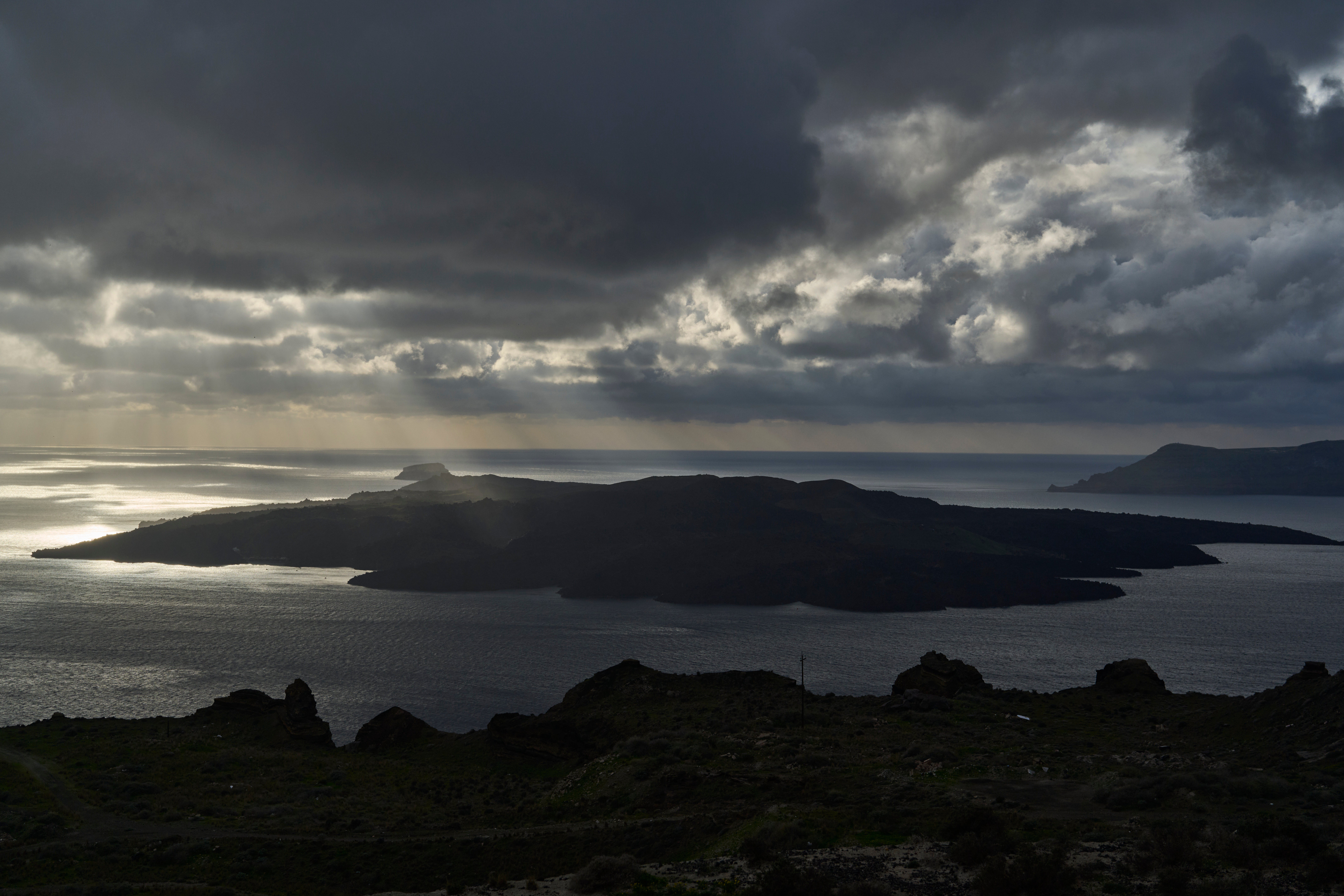 Sun rays illuminate the volcanic islet of Nea Kameni, part of the earthquake-struck island of Santorini