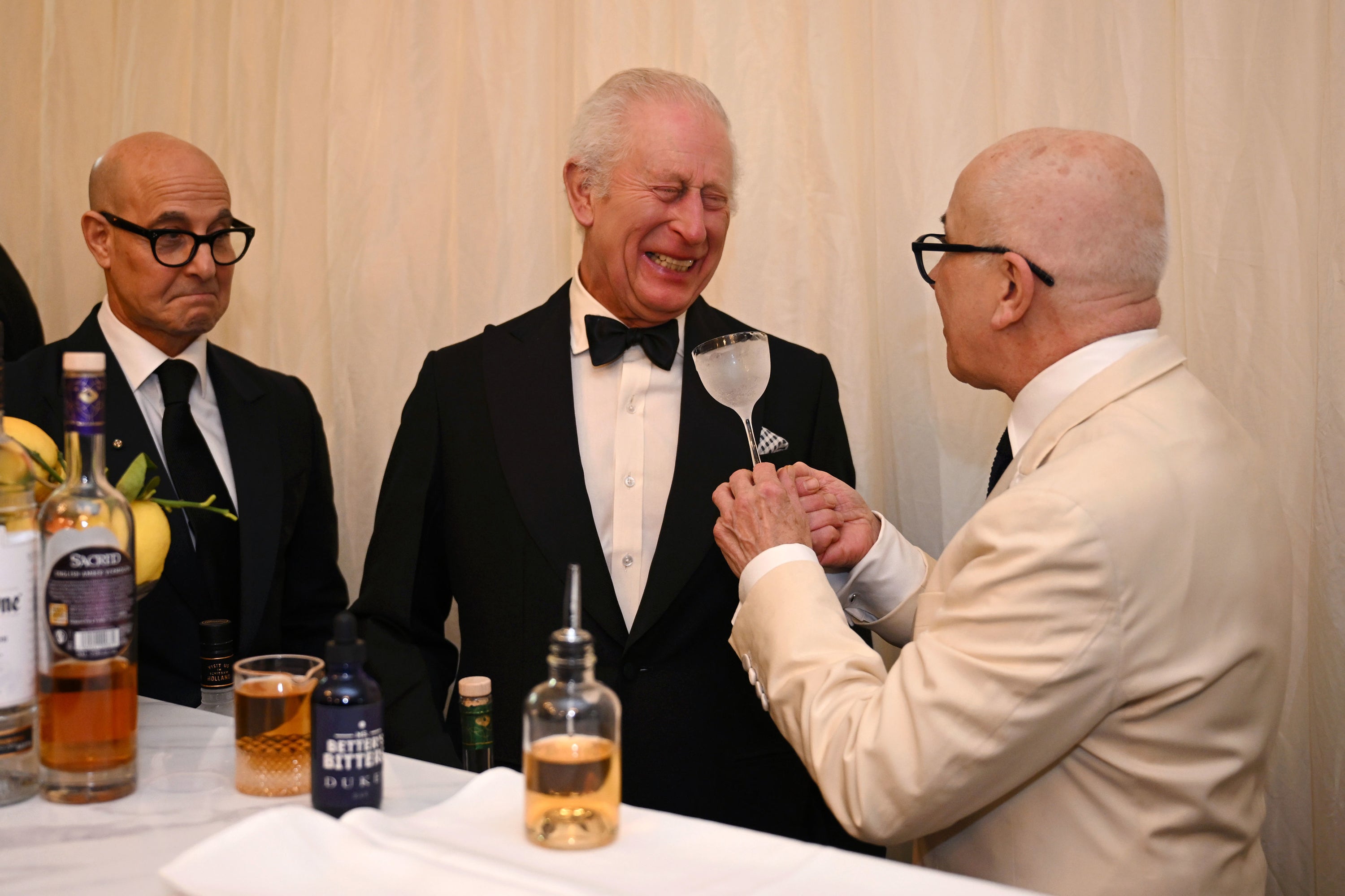 King Charles laughs with mixologist Alessandro Palazzi while actor Stanley Tucci watches on