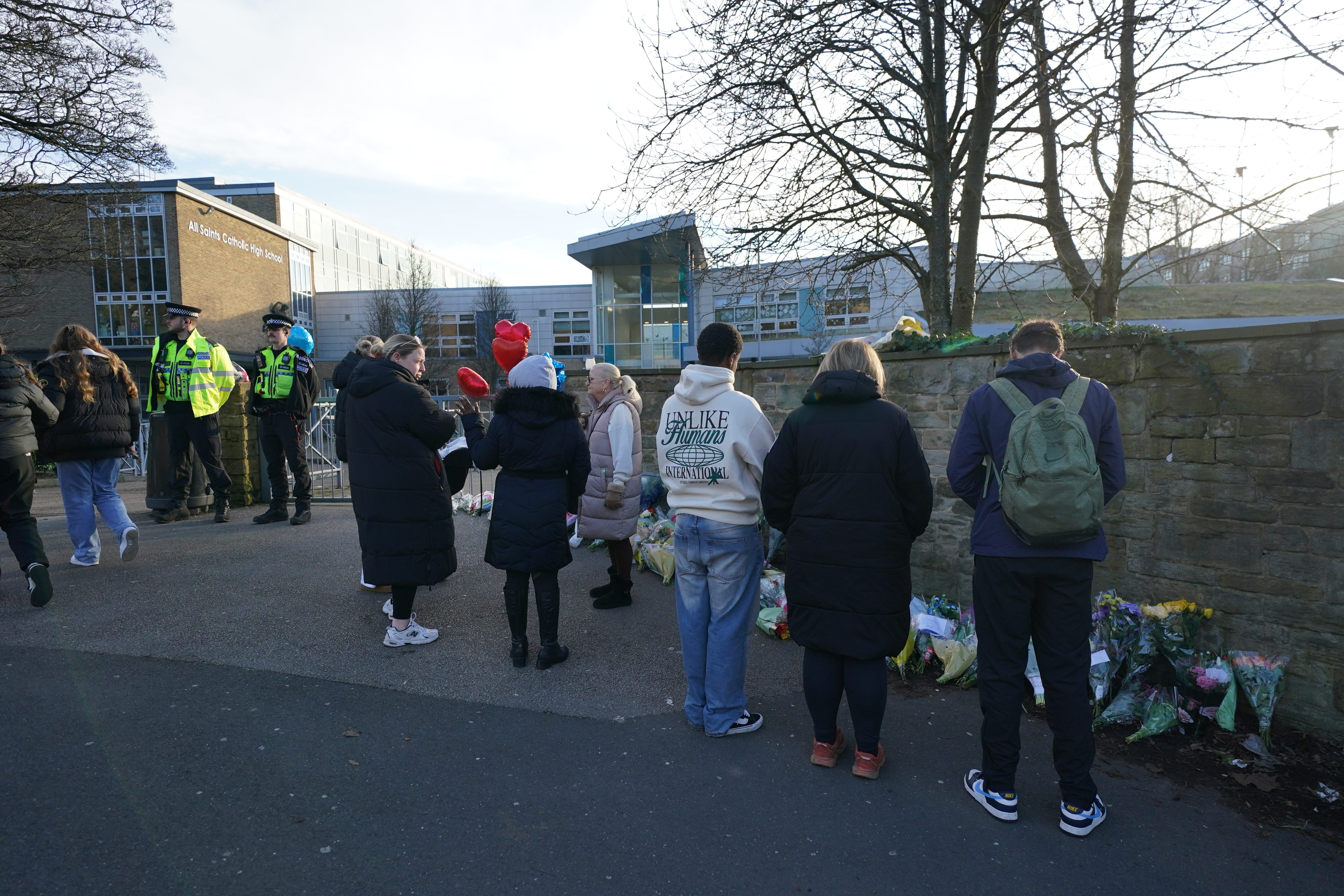 Police officers and floral tributes outside All Saints Catholic High School (PA)