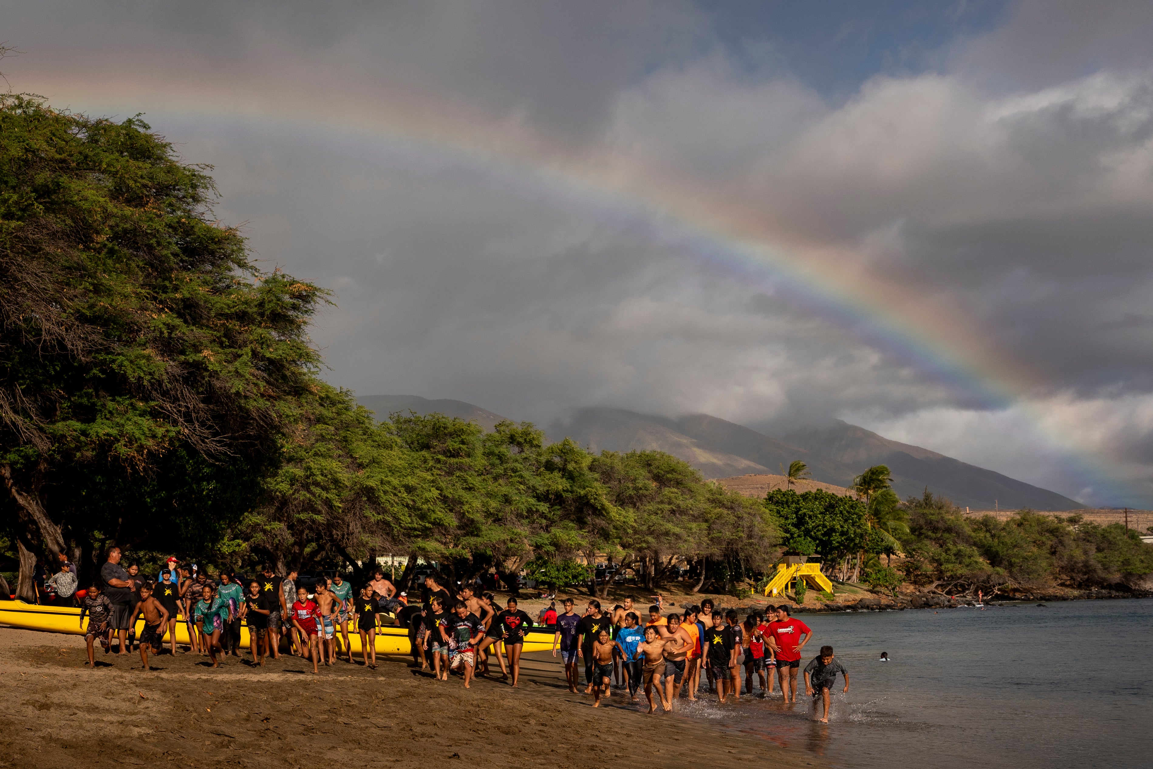 Members of the Napili Canoe Club run sprints on the beach as a rainbow forms nearby on Monday, July 8, 2024, at Hanakao’