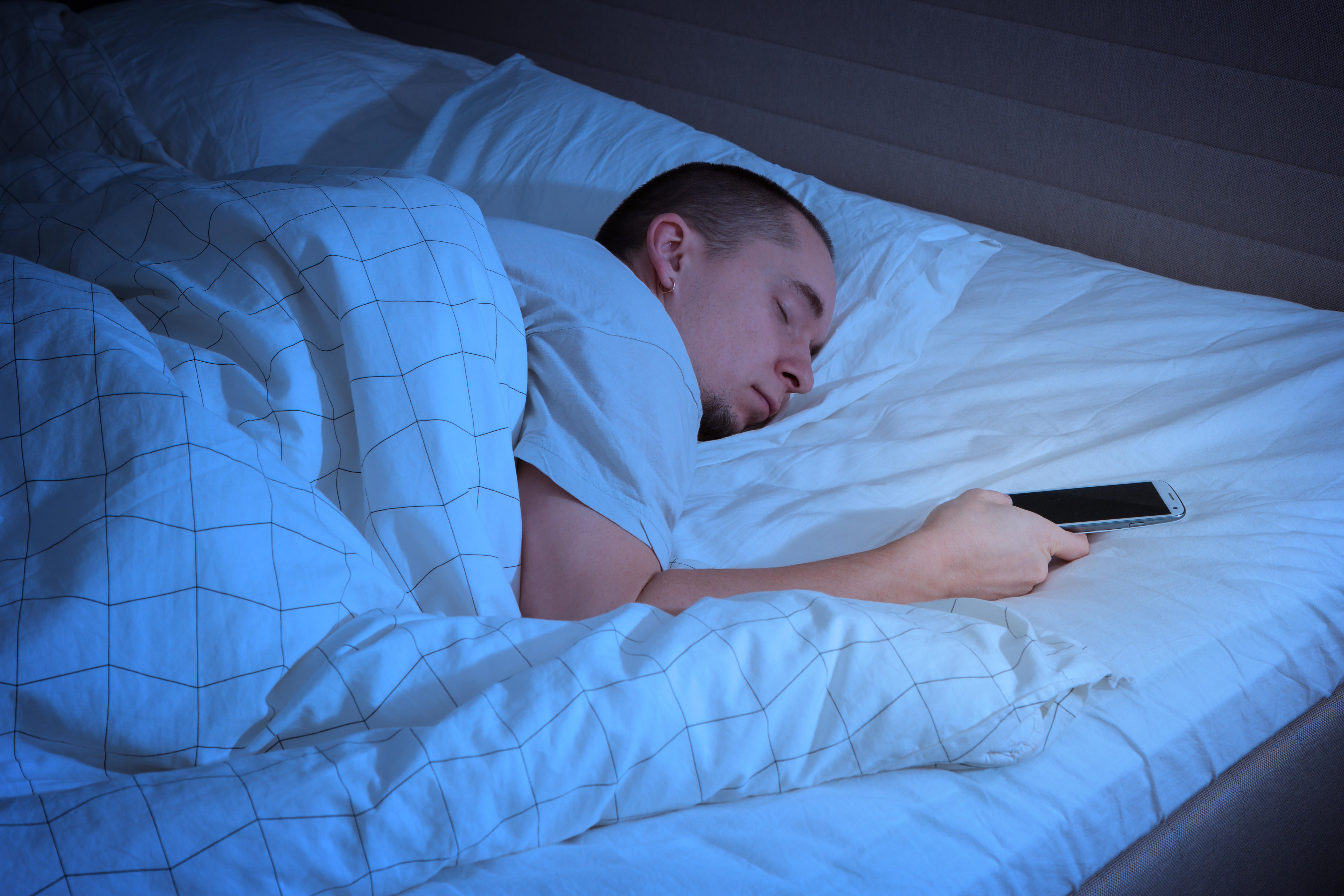 EFD6N2 Man sleeping in bed and holding a mobile phone. Concept photo of smartphone addiction.