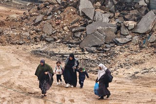 Palestinian women and children walk through the mud departing for safety during an Israeli raid at Alfara refugee camp near Tuba