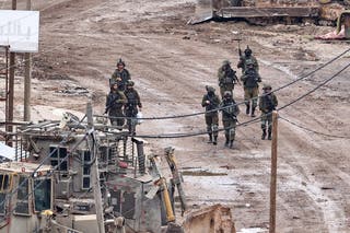 Israeli soldiers walk down the street while raiding at Alphara camp