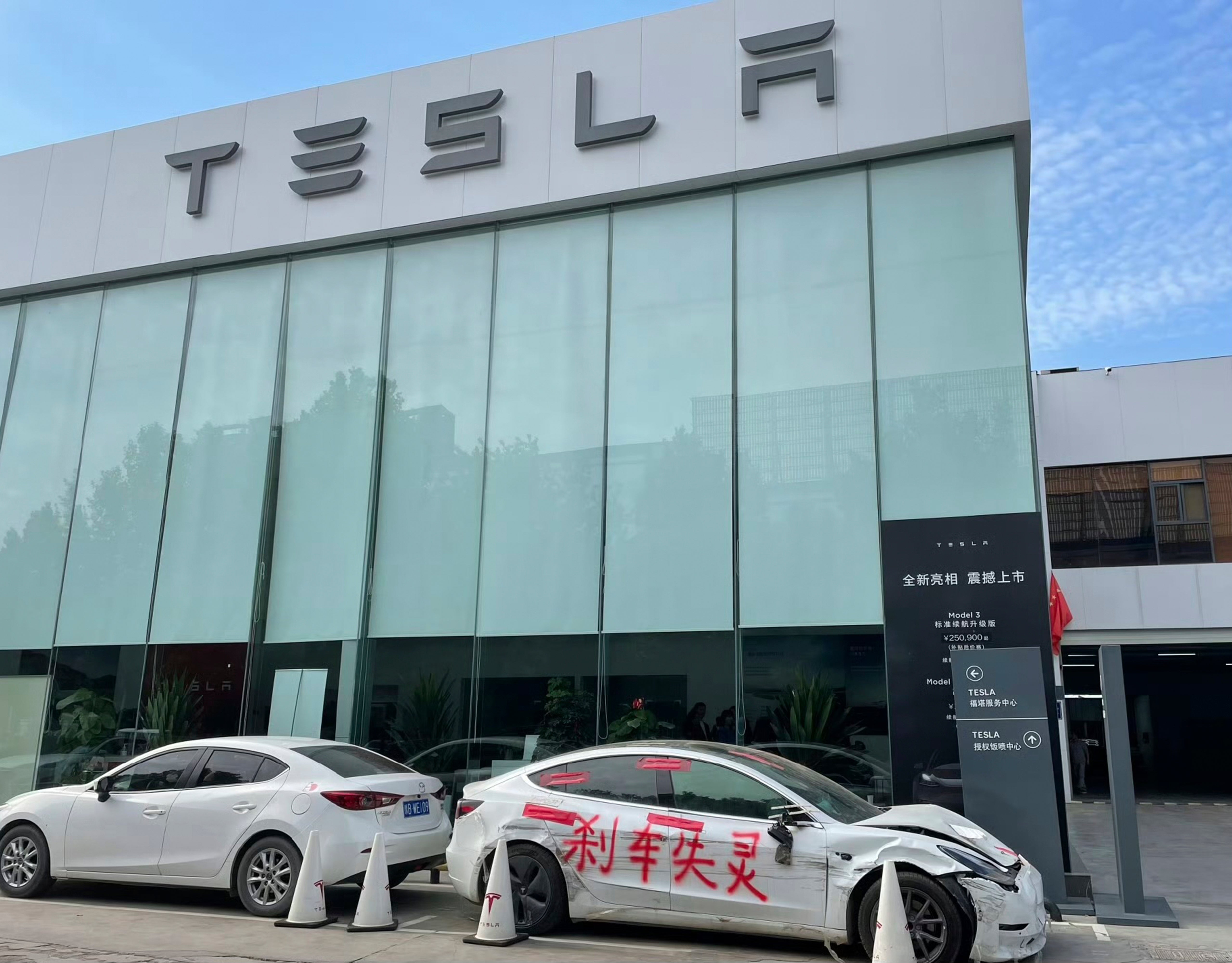 This photo provided by Zhang Yazhou shows her damaged Tesla Model 3, right, parked outside of the Tesla dealership in Zhengzhou, the capital of central China’s Henan province, on March 10, 2021. The car was painted with the phrase, ‘Brakes fail’