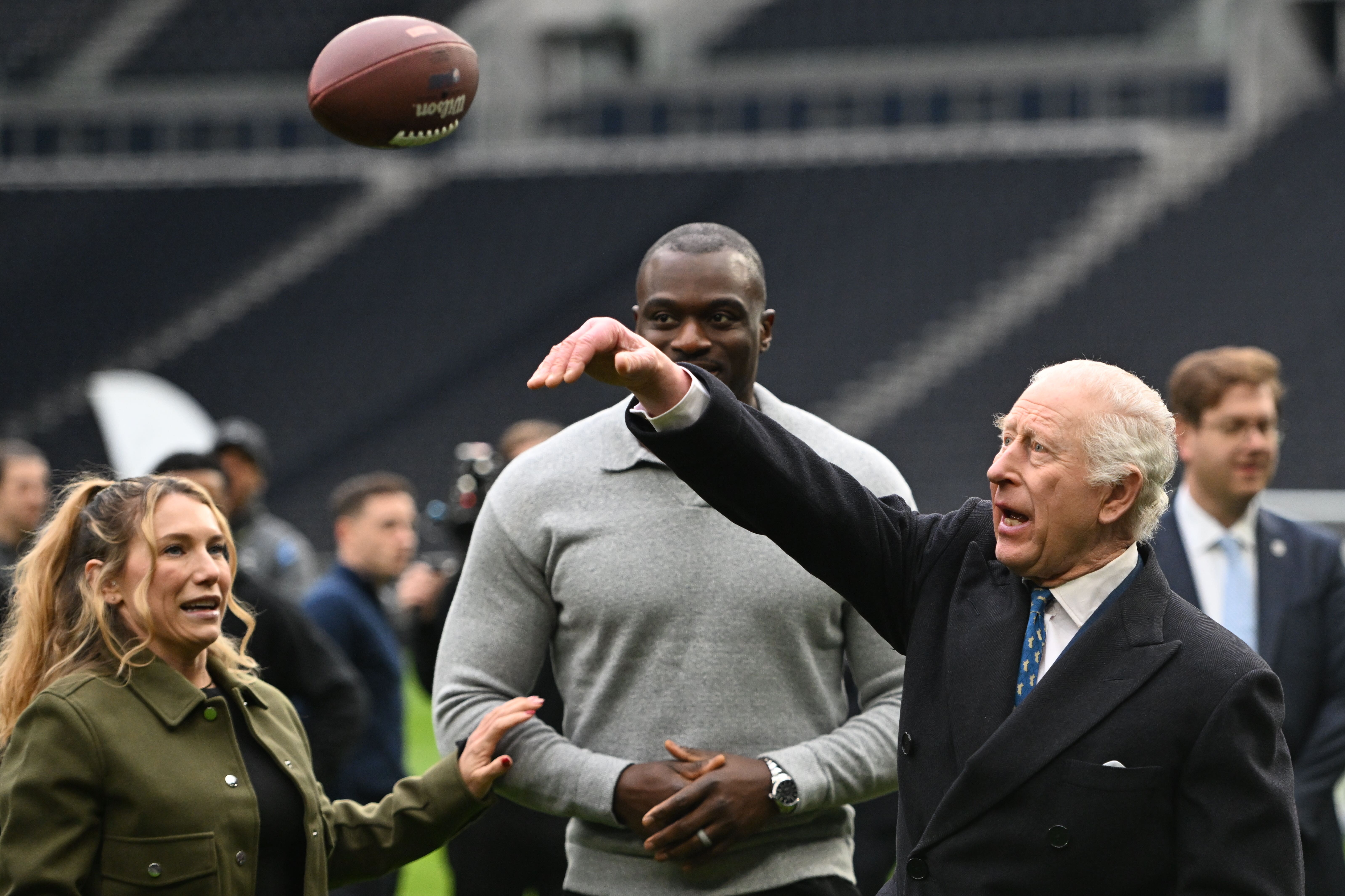 The King is taught how to throw an American Football by Phoebe Schecter (left) and Efe Obada (Eddie Mulholland/Daily Telegraph/PA)