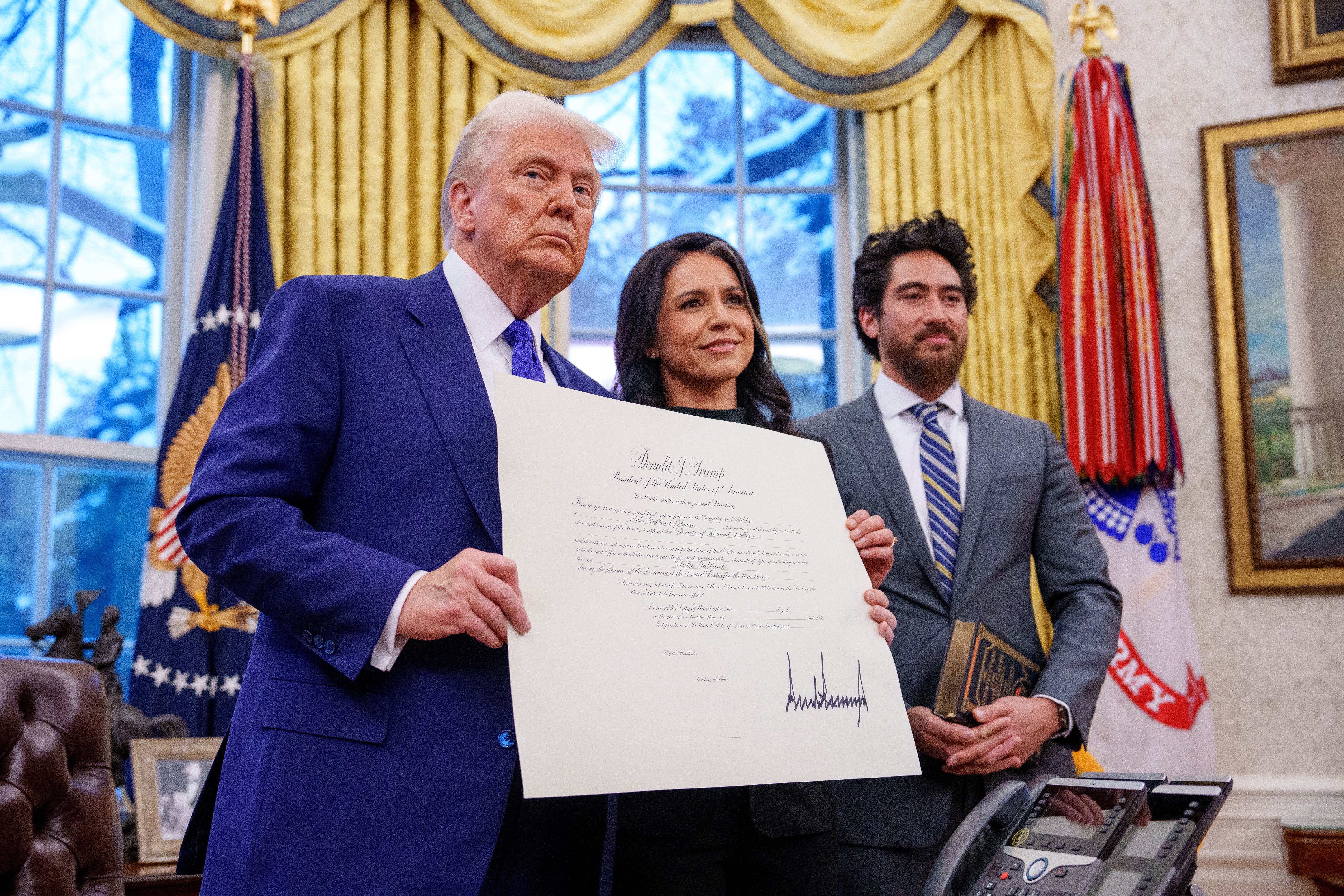 Donald Trump, accompanied by Tulsi Gabbard and her husband Abraham Williams, holds up Gabbard's commission for her new role as Director of National Intelligence after she was sworn in, in the Oval Office at the White House on February 12, 2025 in Washington, DC.