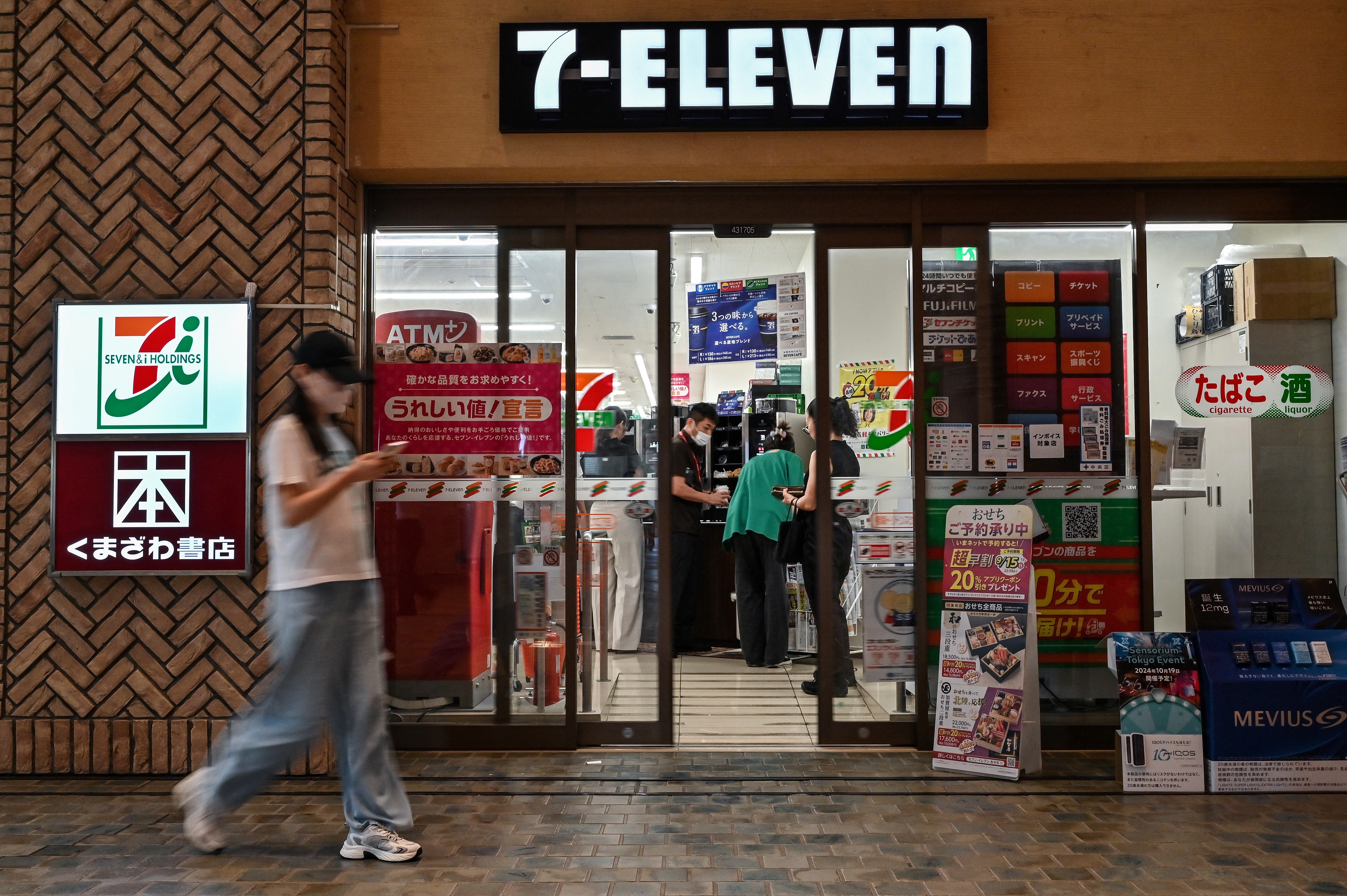 This photo taken on September 13, 2024 shows a woman walking past a 7-Eleven convenience store in Tokyo