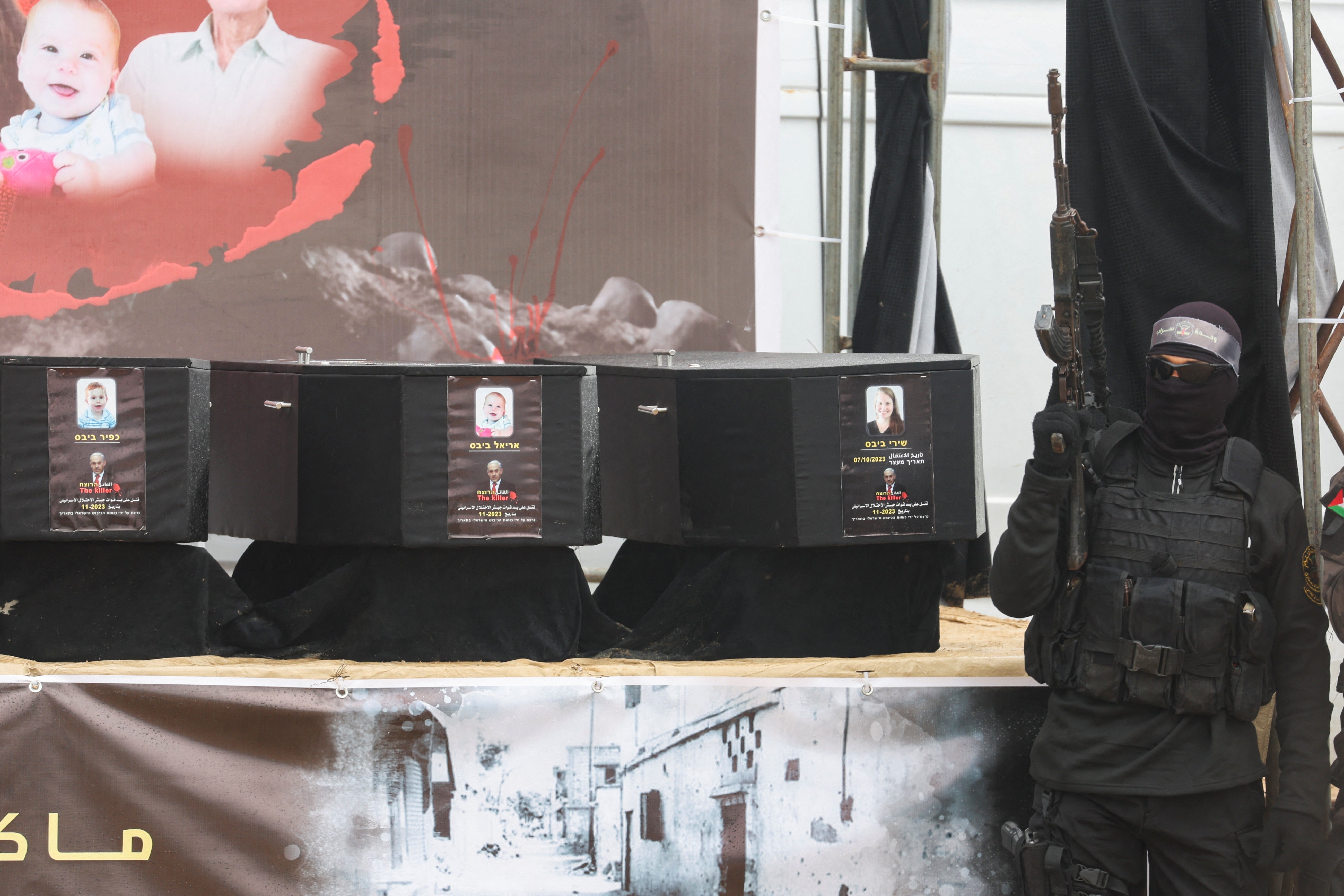 A Palestinian militant stands near coffins during the handover of deceased Israeli hostages Shiri Bibas and her children Kfir and Ariel